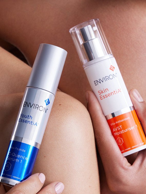 Environ skincare, AVST and eye gel. Malta. A person holding two skincare products next to their shoulder and arm, with a close-up of their skin visible.