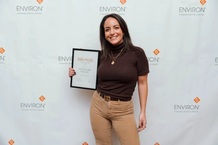 Person holding a bronze award certificate against an Environ-branded backdrop.