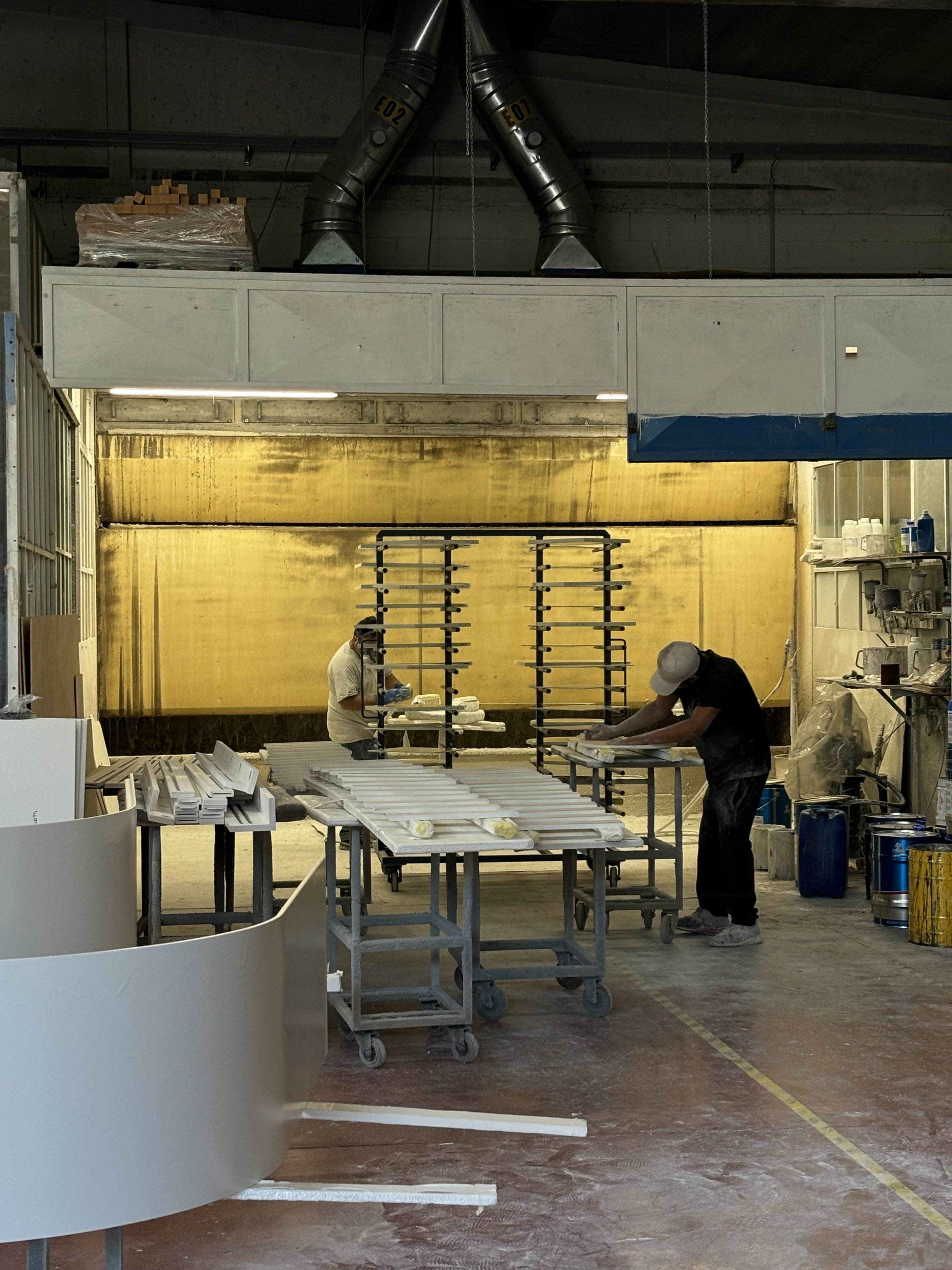 Atelier, des personnes manipules des pièces de mobilier devant une cabine de thermolaquage