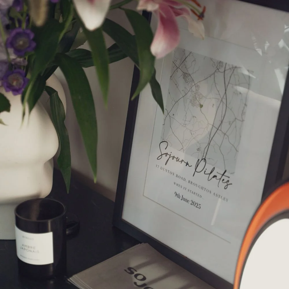 Framed map of Sojourn Pilates studio at 17 Dunton Road, Broughton Astley, displayed on a shelf with a candle and fresh flowers.