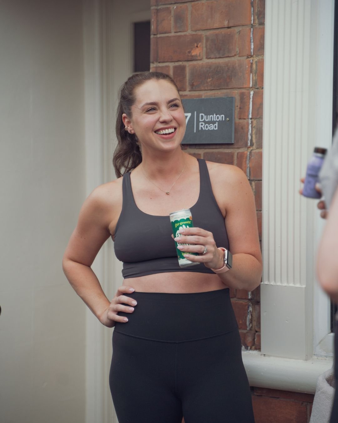 Smiling Sojourn Pilates member outside the studio entrance at 17 Dunton Road in Broughton Astley, post-class drink in hand.