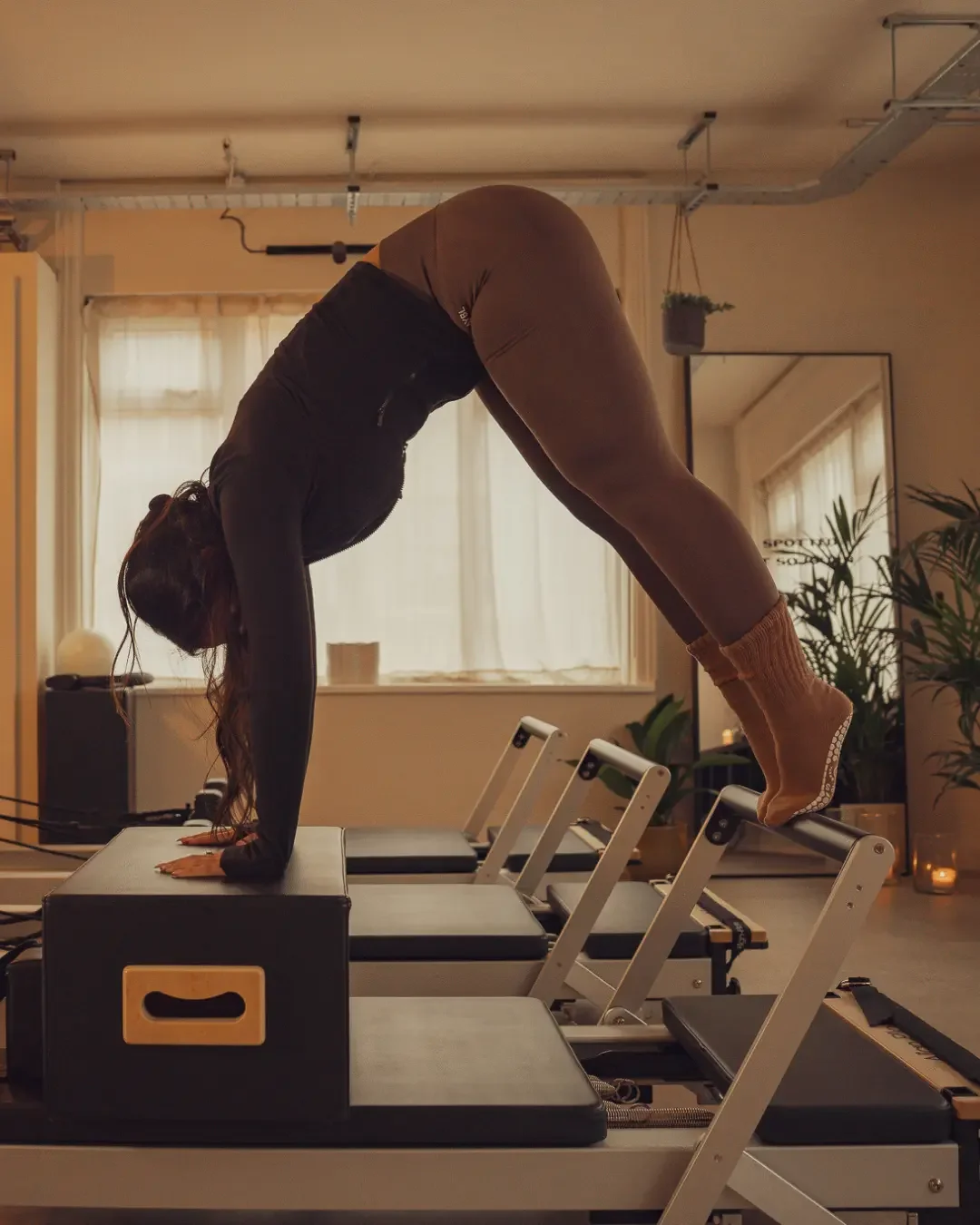 Warmly lit photo showing a woman performing a Pilates pike on the reformer Pilates short box and footbar at Sojourn Pilates, boutique studio in Leicestershire