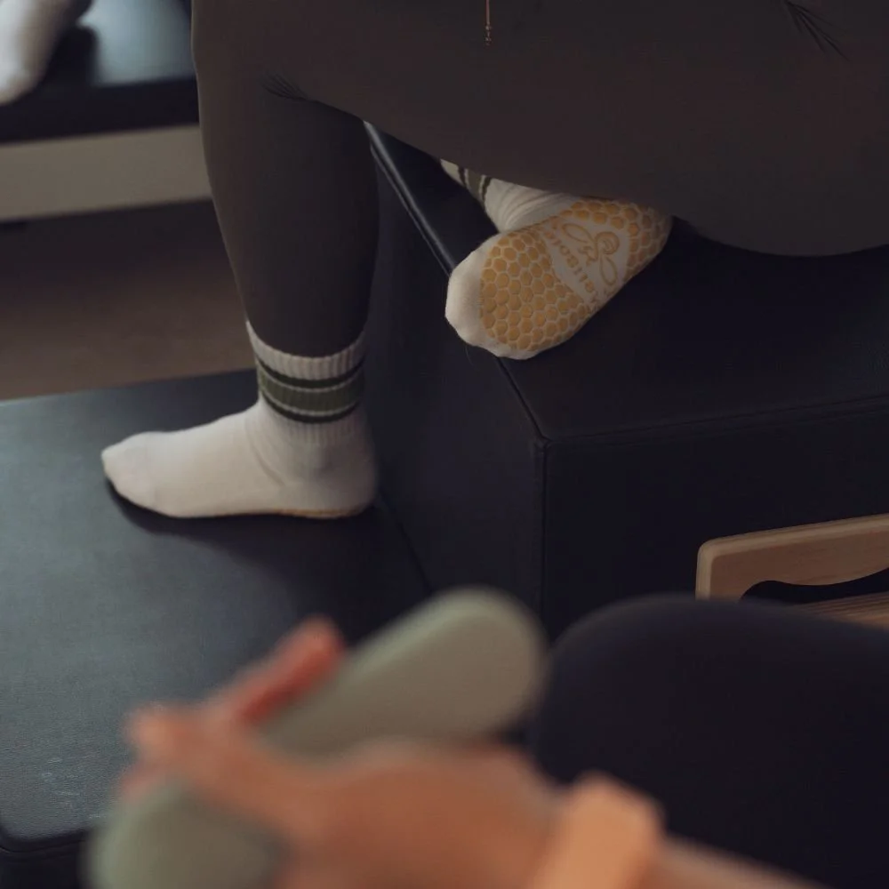 Close-up of branded grip socks worn by a client on the studio floor at Sojourn Pilates.