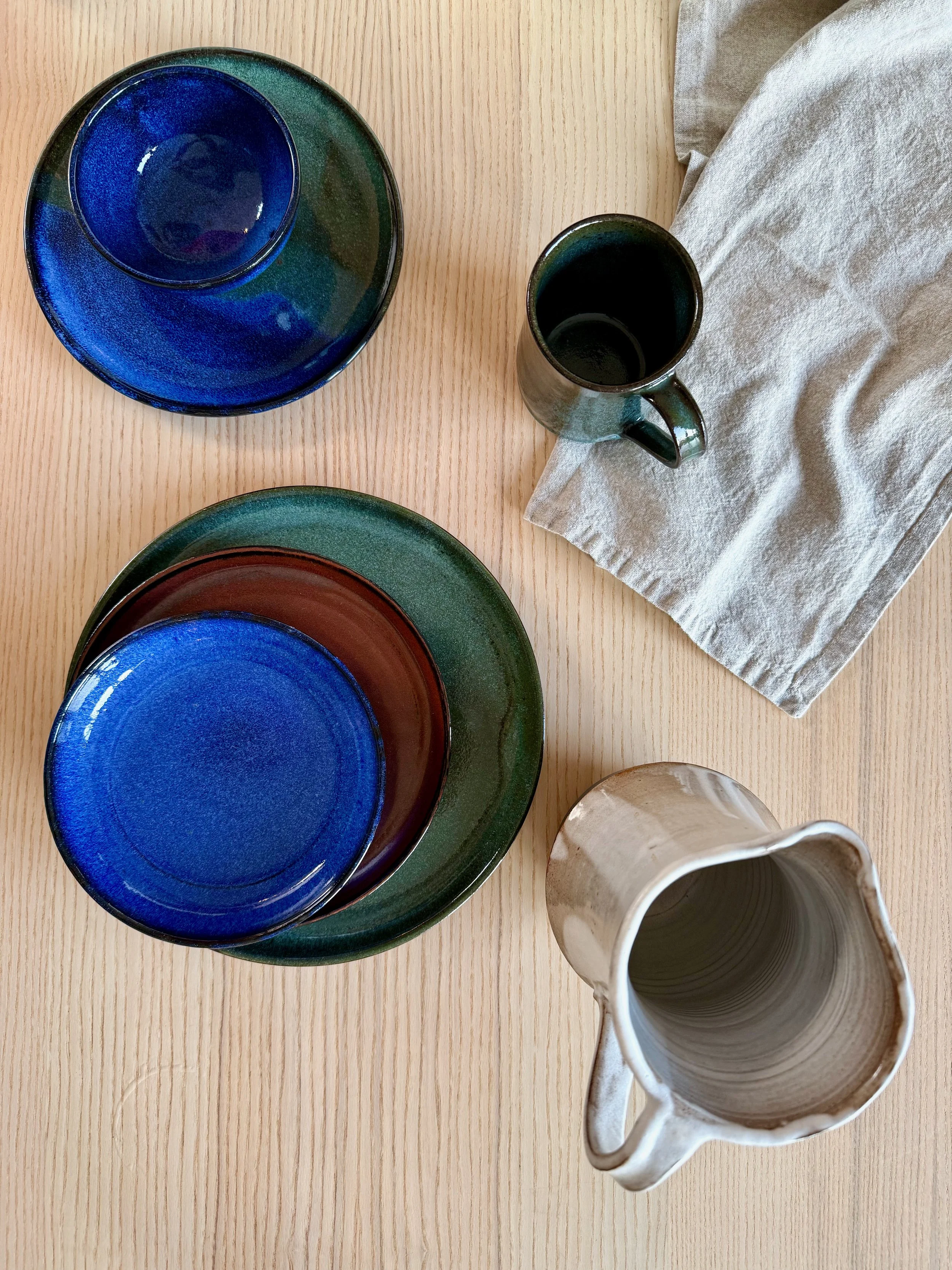 handmade plates in blue, red, and green and handmade pitcher photographed from above