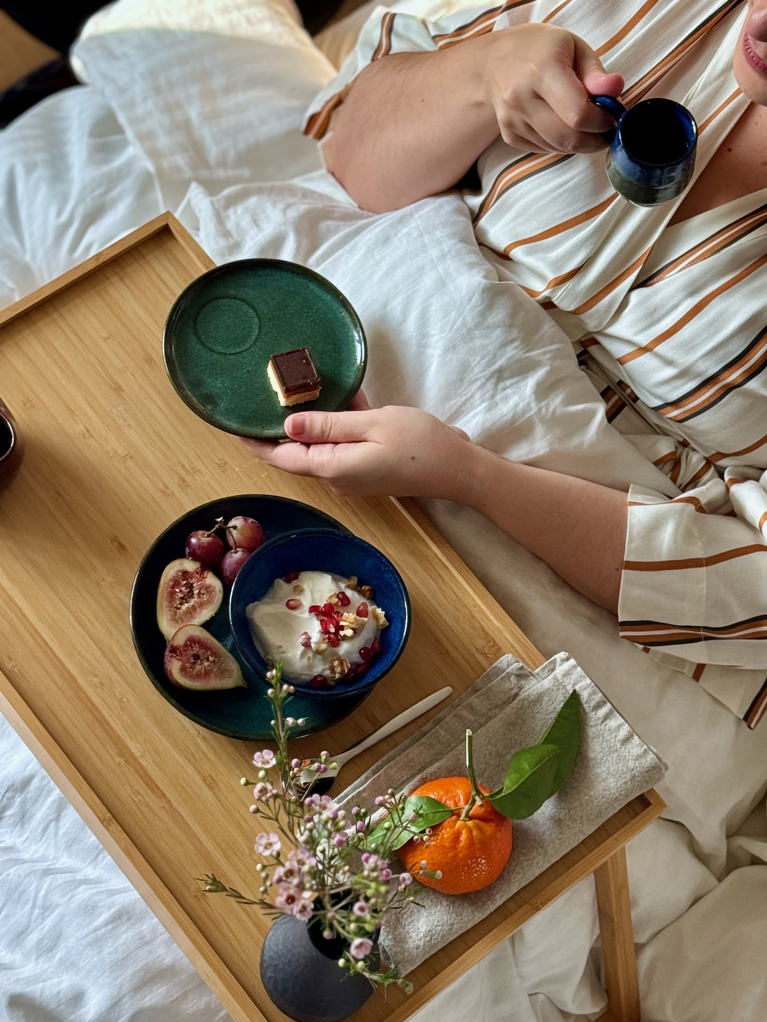 A handmade breakfast in bed set including green ceramic doppio cup and saucer, blue yogurt bowl, green fruit bowl, and black vase.