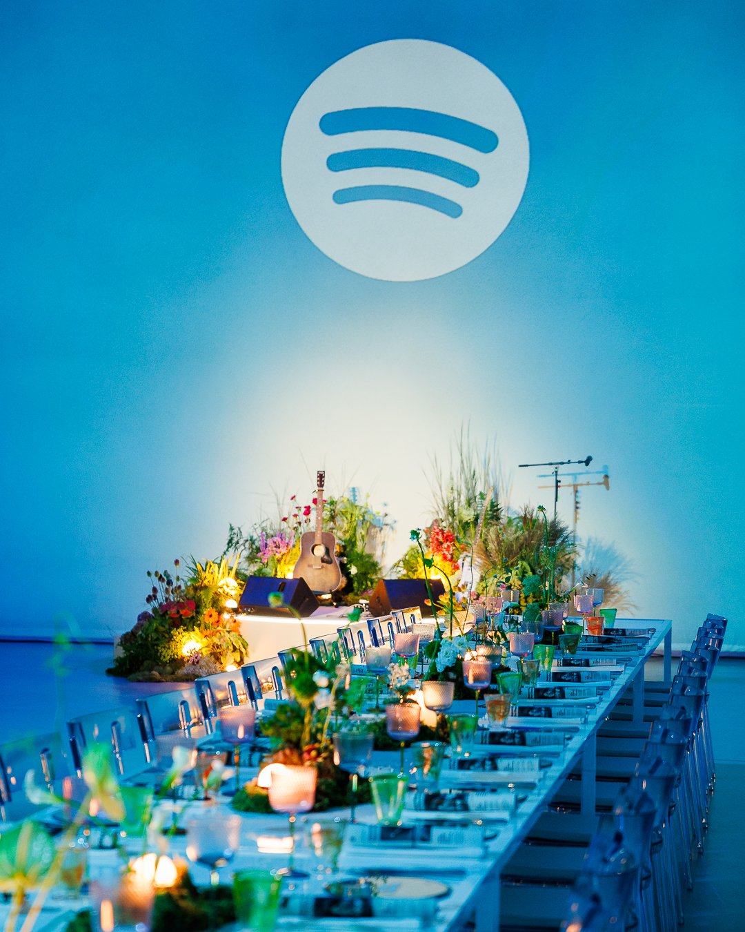 Concert stage decorated with flowers, guitars, and microphones, illuminated by soft lighting, with a Spotify logo projected on the wall.