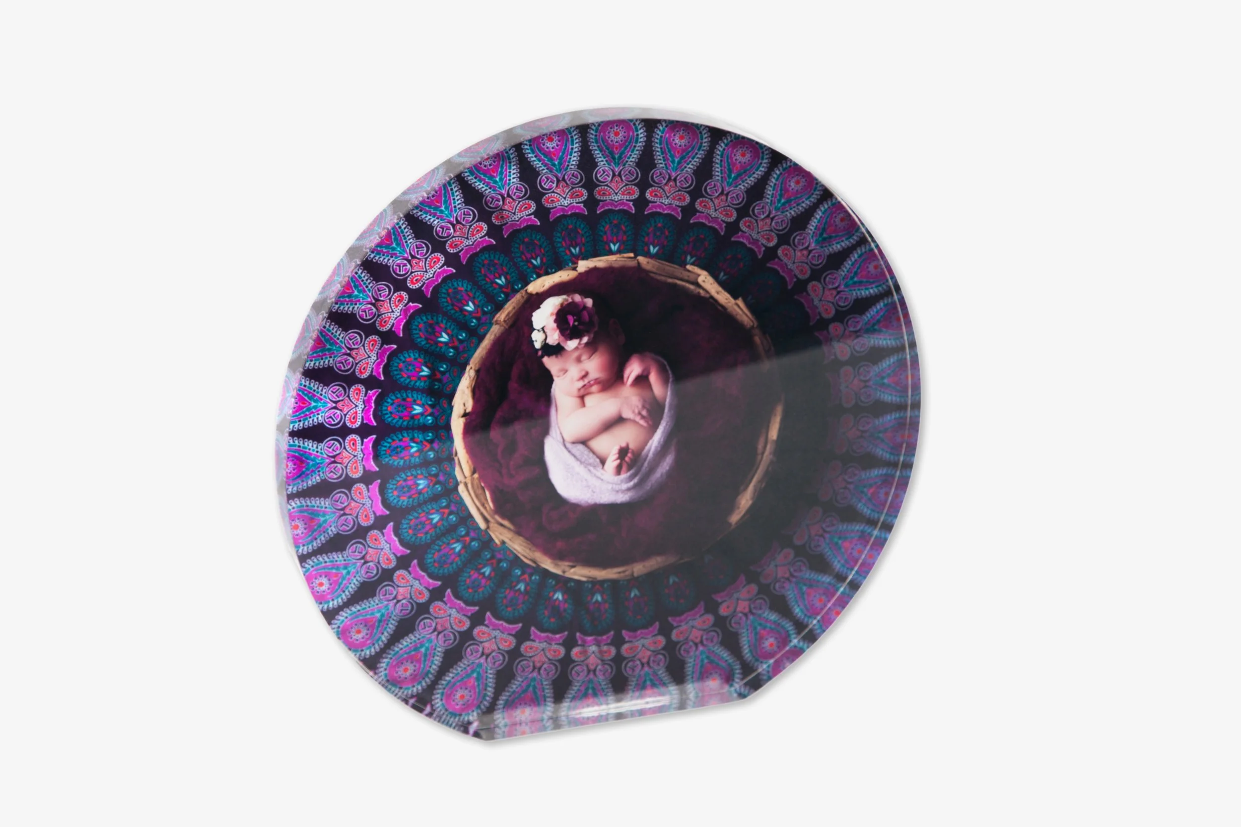 Baby lying in a basket inside a glass case, surrounded by colorful fabric with a paisley pattern.