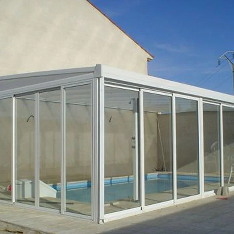 Estructura de vidrio para un área de piscina cubierta, ubicada en el exterior de una casa.