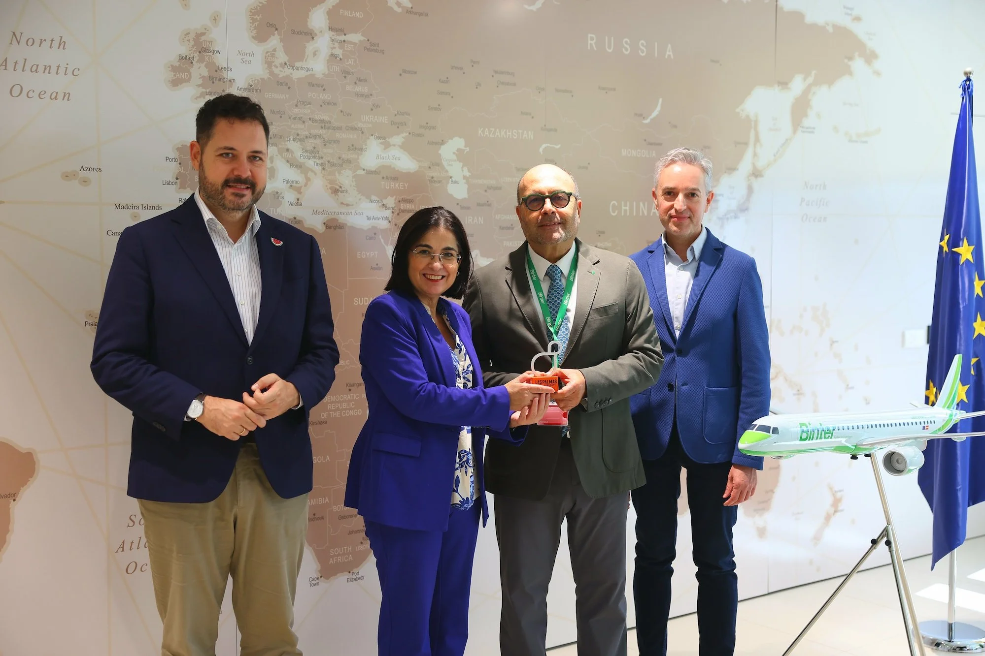 Josué Íñiguez, Carolina Darias, Santiago Guerra y José Luis Pérez Pont posan ante un gran mapa del mundo, junto a la bandera europea y una maqueta de un avión de Binter