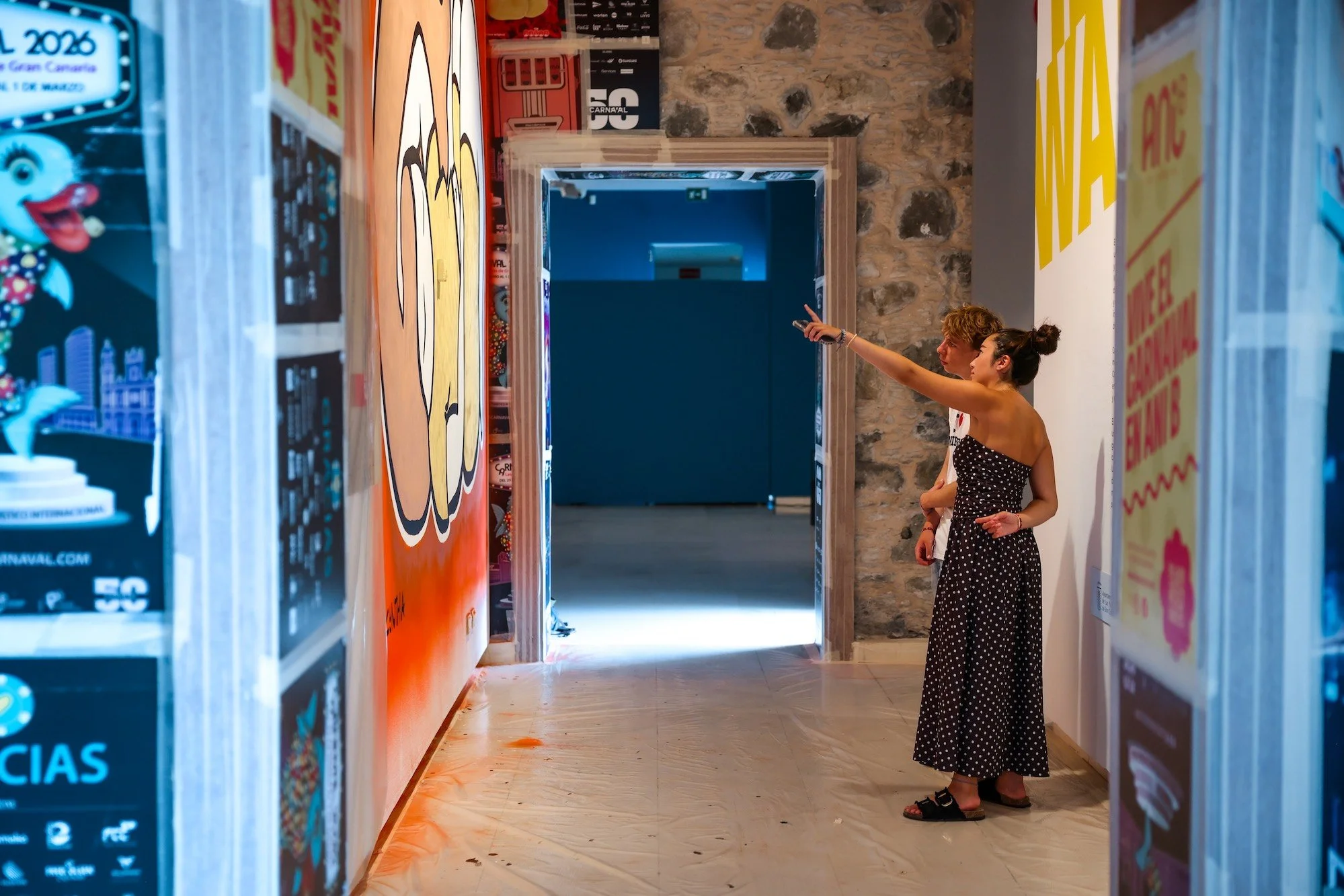 Dos visitantes observan la exposición de carteles de Carnaval en un pasillo del Castillo de Mata