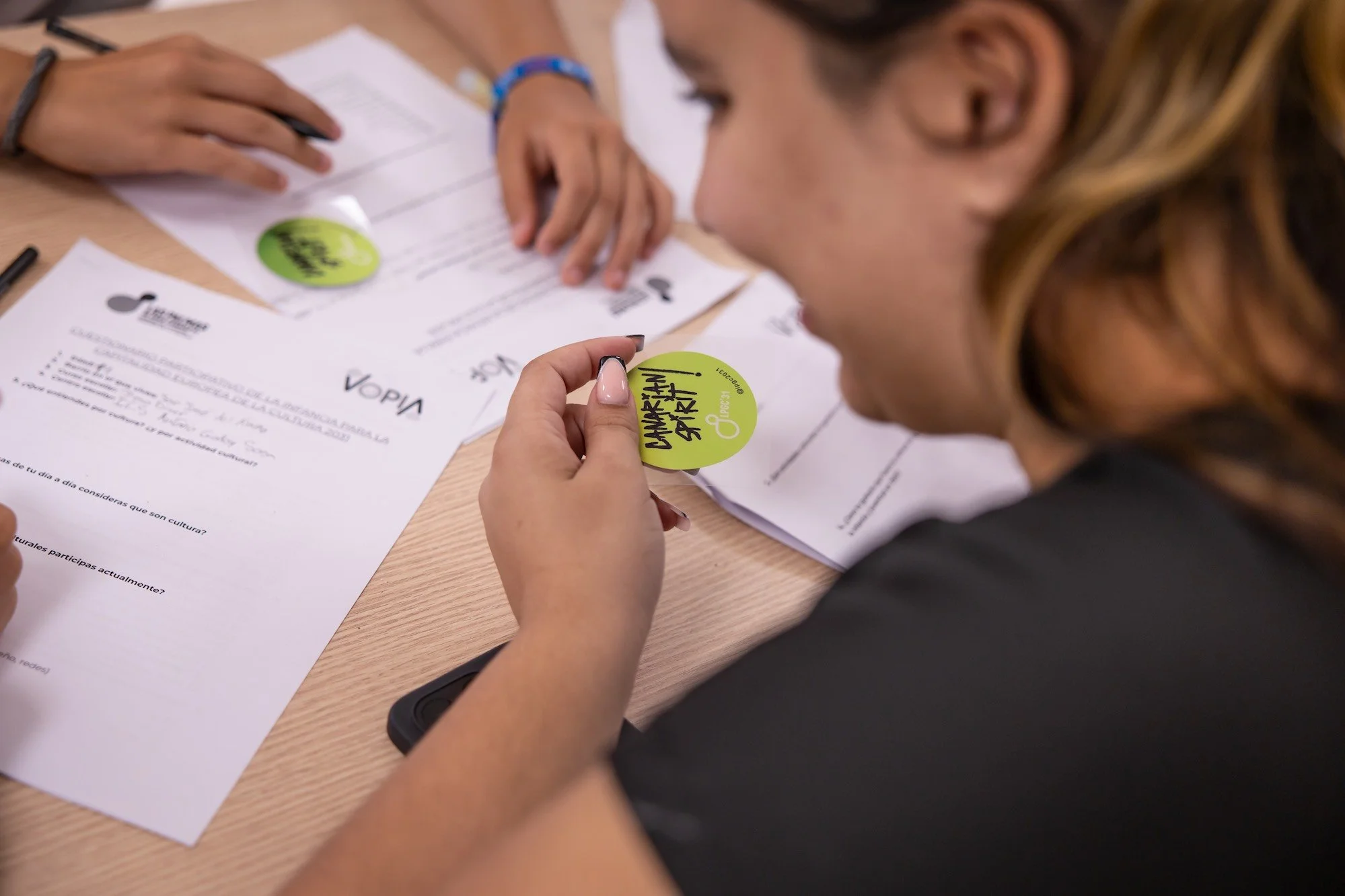 Detalle de manos completando el cuestionario participativo de la infancia sobre cultura, con una pegatina de la candidatura LPGC'31