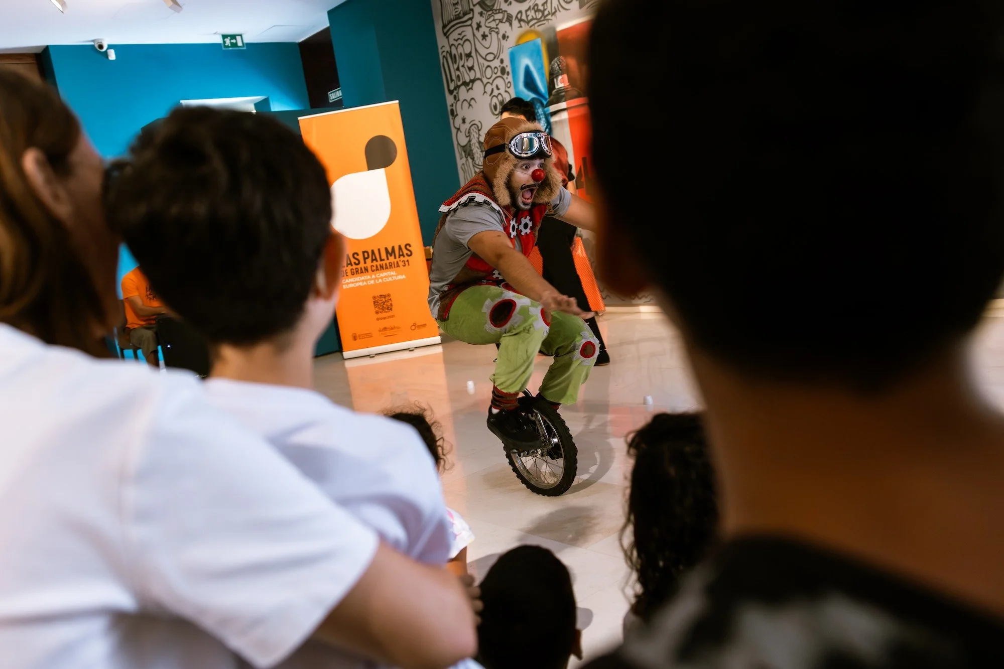 Joven artista haciendo malabares sobre un monociclo ante niños durante un taller de circo social de Circus 4 All