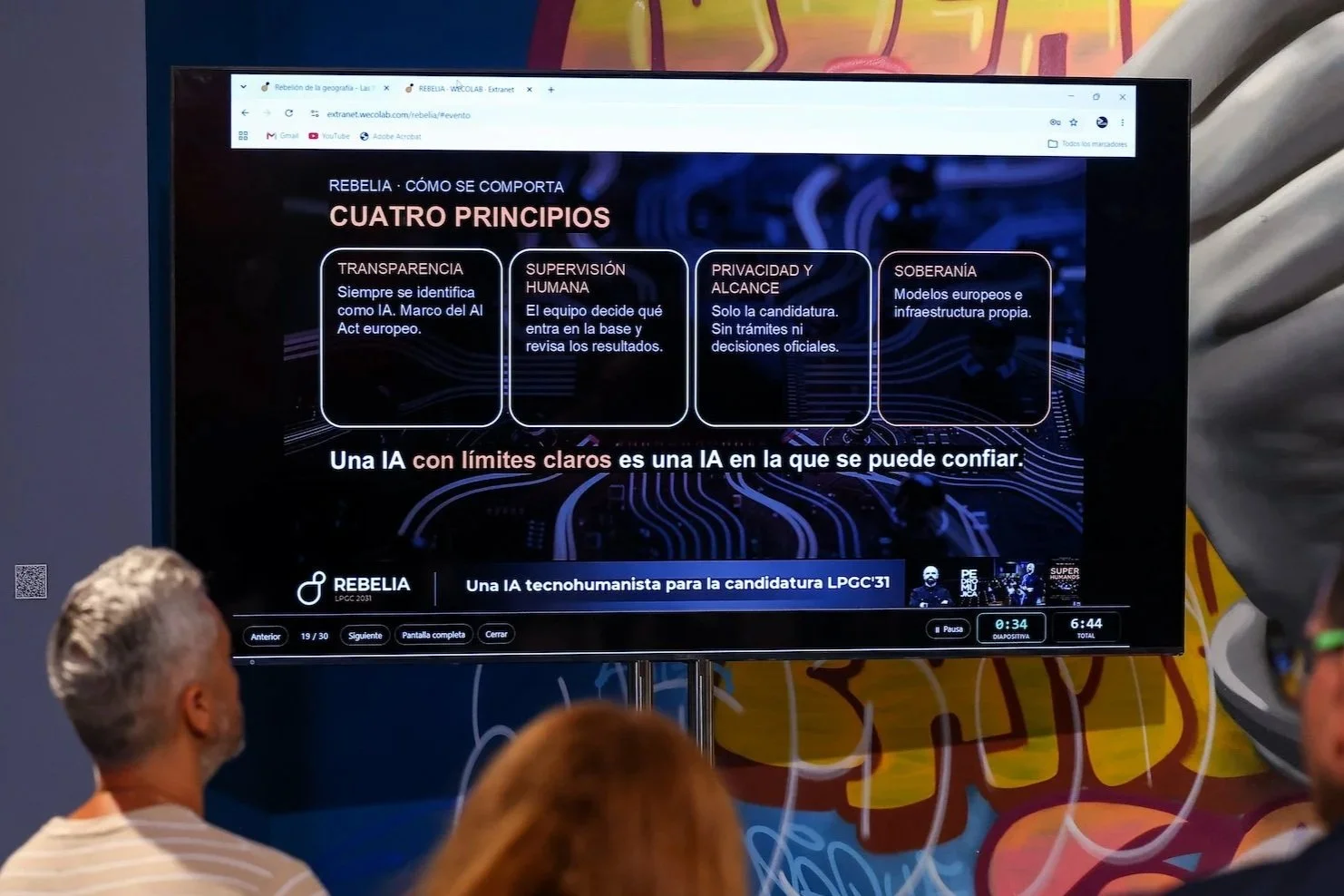 Pantalla con una diapositiva de REBELIA titulada ‘Cuatro principios’: transparencia, supervisión humana, privacidad y alcance, y soberanía, con dos espectadores de espaldas en primer plano