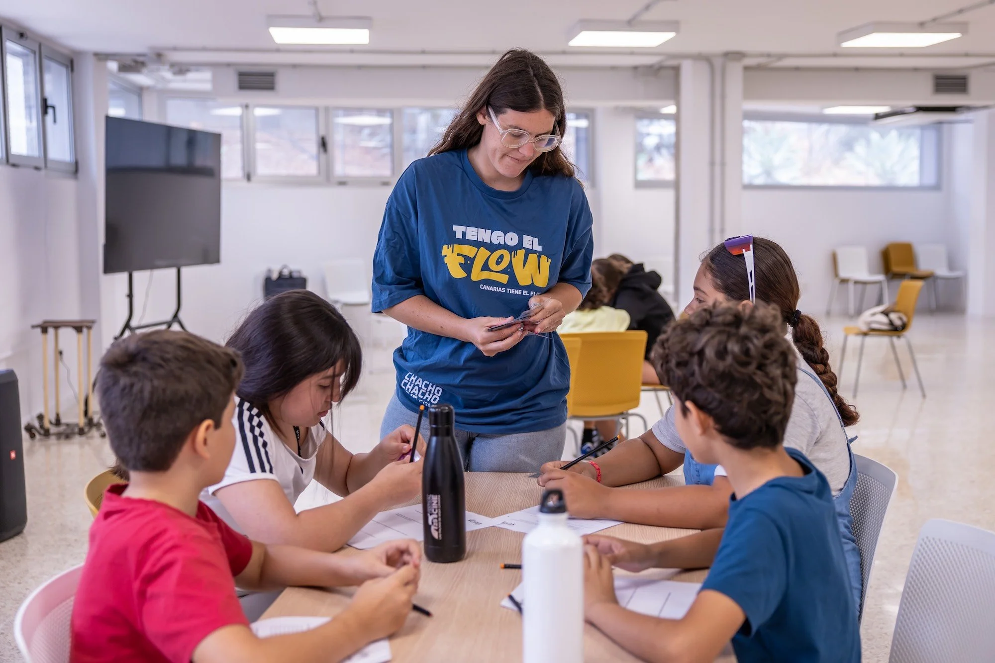 Una persona monitora ayuda a un grupo de participantes infantiles a completar sus fichas durante una actividad del campus VOPIA Urban Lab