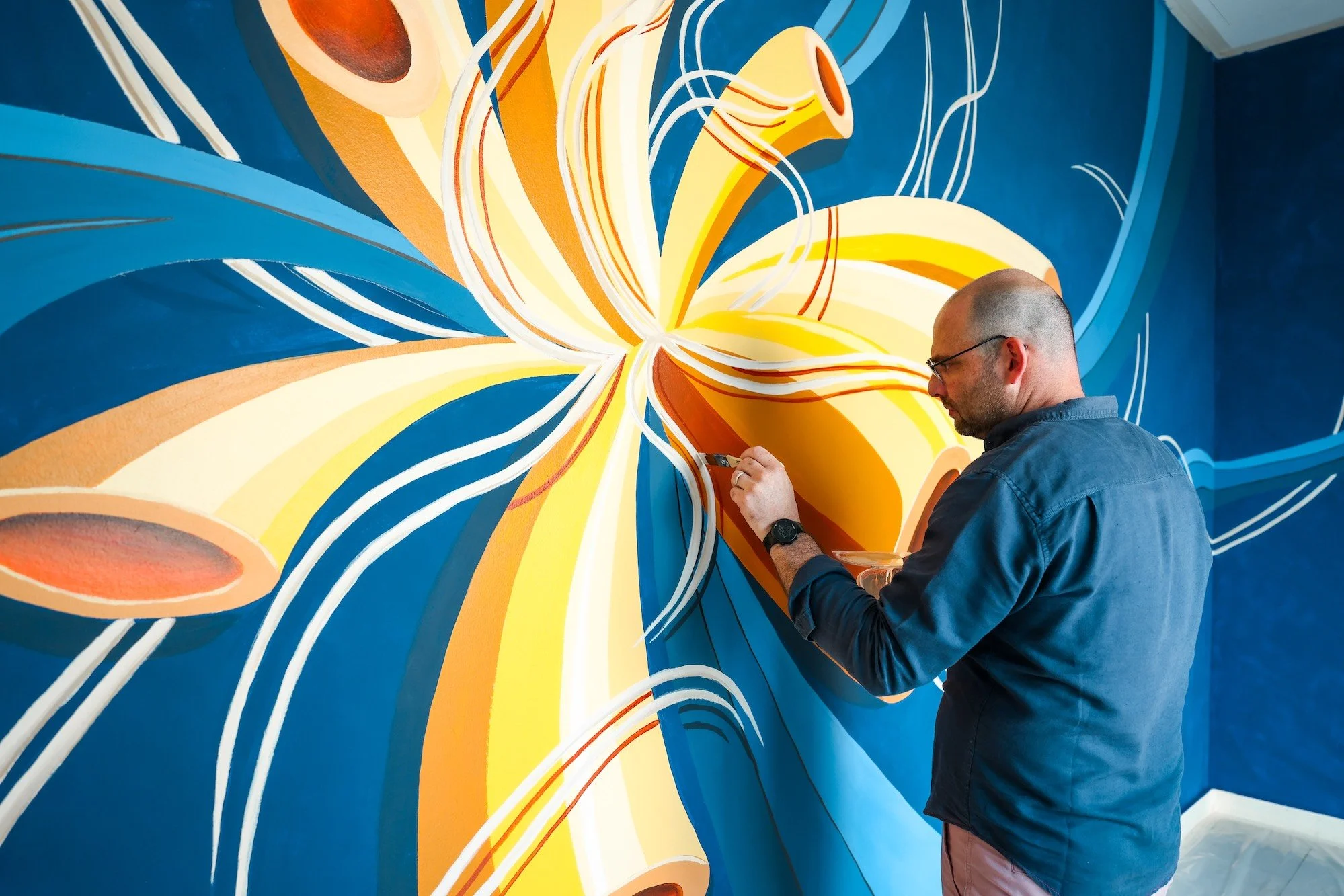 El artista Jason Joe Farrugia pinta un mural abstracto de formas florales en tonos azules y amarillos en el Castillo de Mata