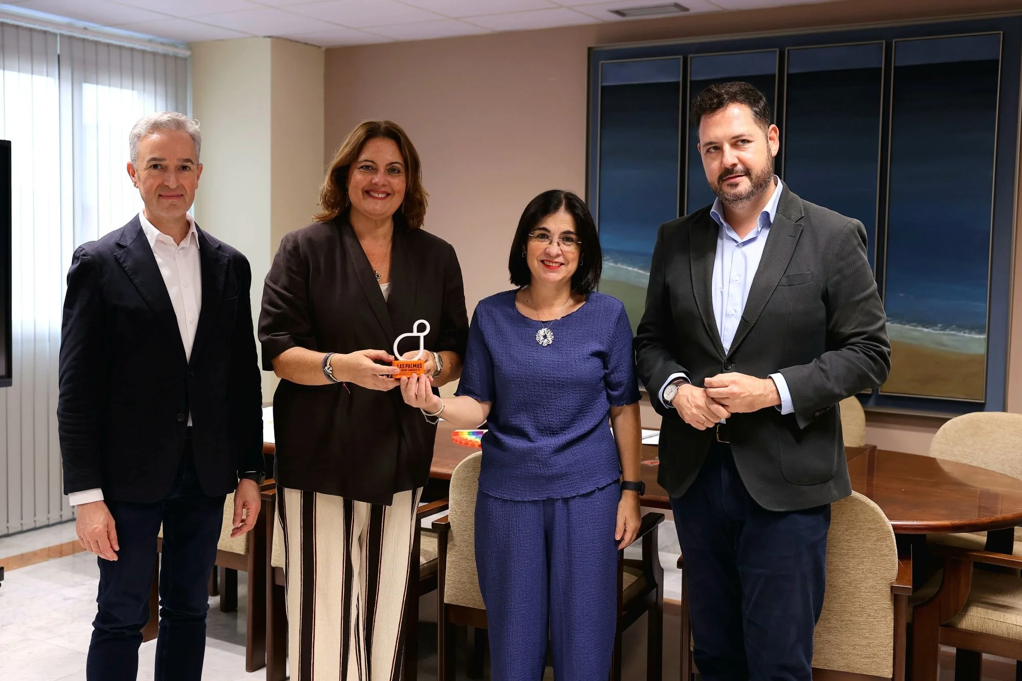 José Luis Pérez Pont, Beatriz Calzada, Carolina Darias y Josué Íñiguez posan en una sala de reuniones; Calzada y Darias sostienen juntas la escultura del símbolo de LPGC’31