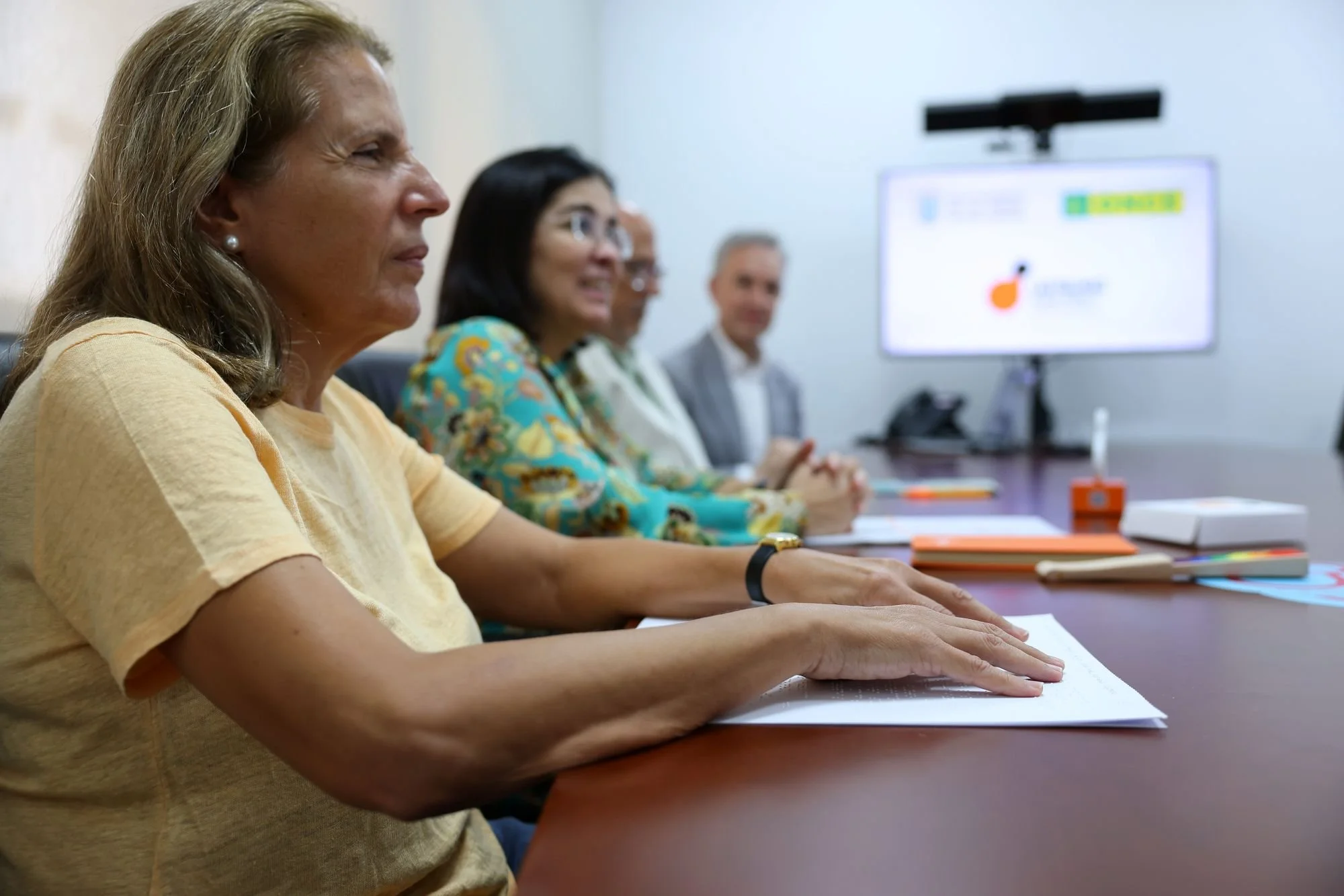 Lucía Martín González lee con las manos el manifiesto en braille, sentada a una mesa de reuniones junto a Carolina Darias y otros asistentes