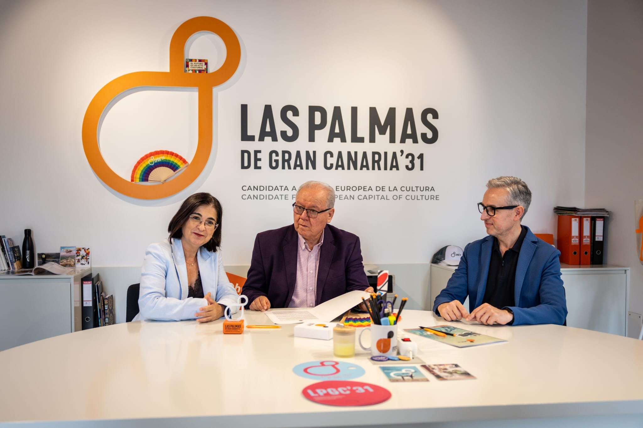 Luis Villa, sentado entre Carolina Darias y José Luis Pérez Pont a una mesa blanca, bajo el logotipo naranja de Las Palmas de Gran Canaria ‘31, con el manifiesto y material de la candidatura sobre la mesa