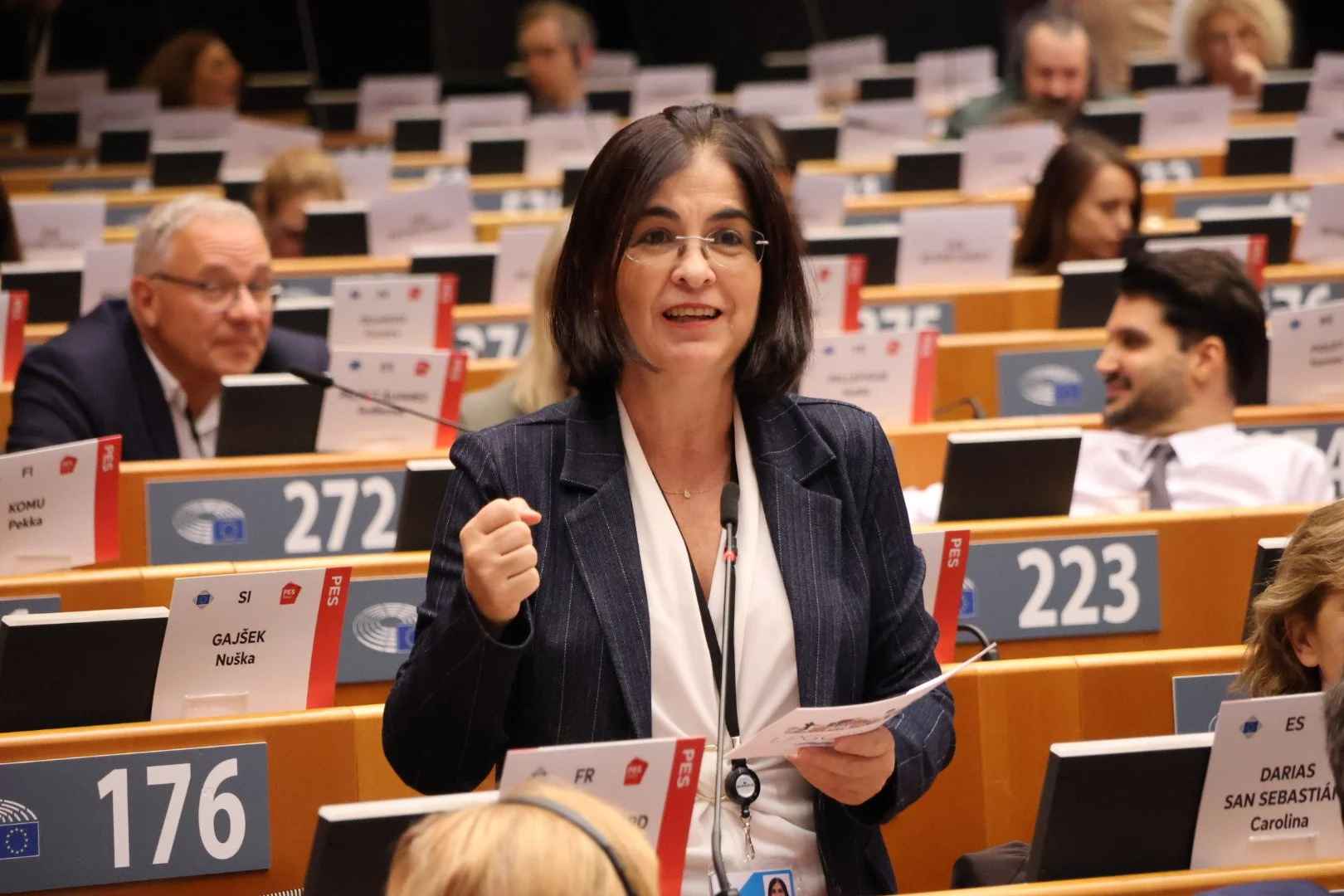 Carolina Darias interviene de pie, con el puño cerrado y un papel en la mano, en el hemiciclo del Comité Europeo de las Regiones, rodeada de escaños numerados y otros miembros sentados