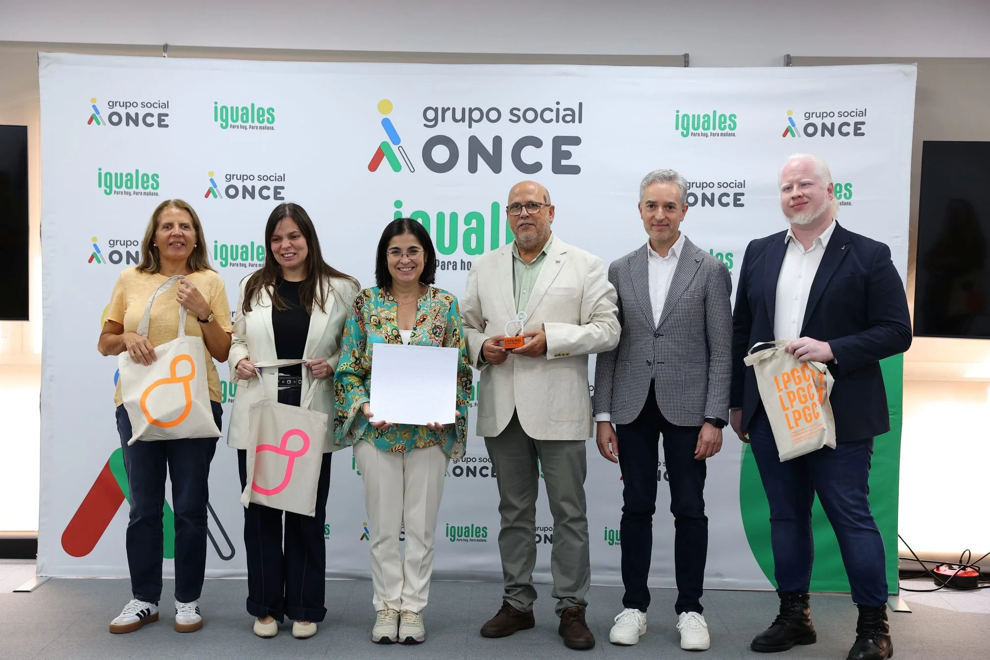 Seis personas posan ante un panel del Grupo Social ONCE; Carolina Darias, en el centro, sostiene el manifiesto firmado, y a su lado un hombre sostiene la escultura del símbolo de LPGC’31