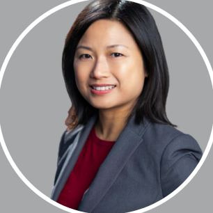 Professional woman with shoulder-length black hair, smiling, wearing a gray blazer and red top, in front of a gray background.
