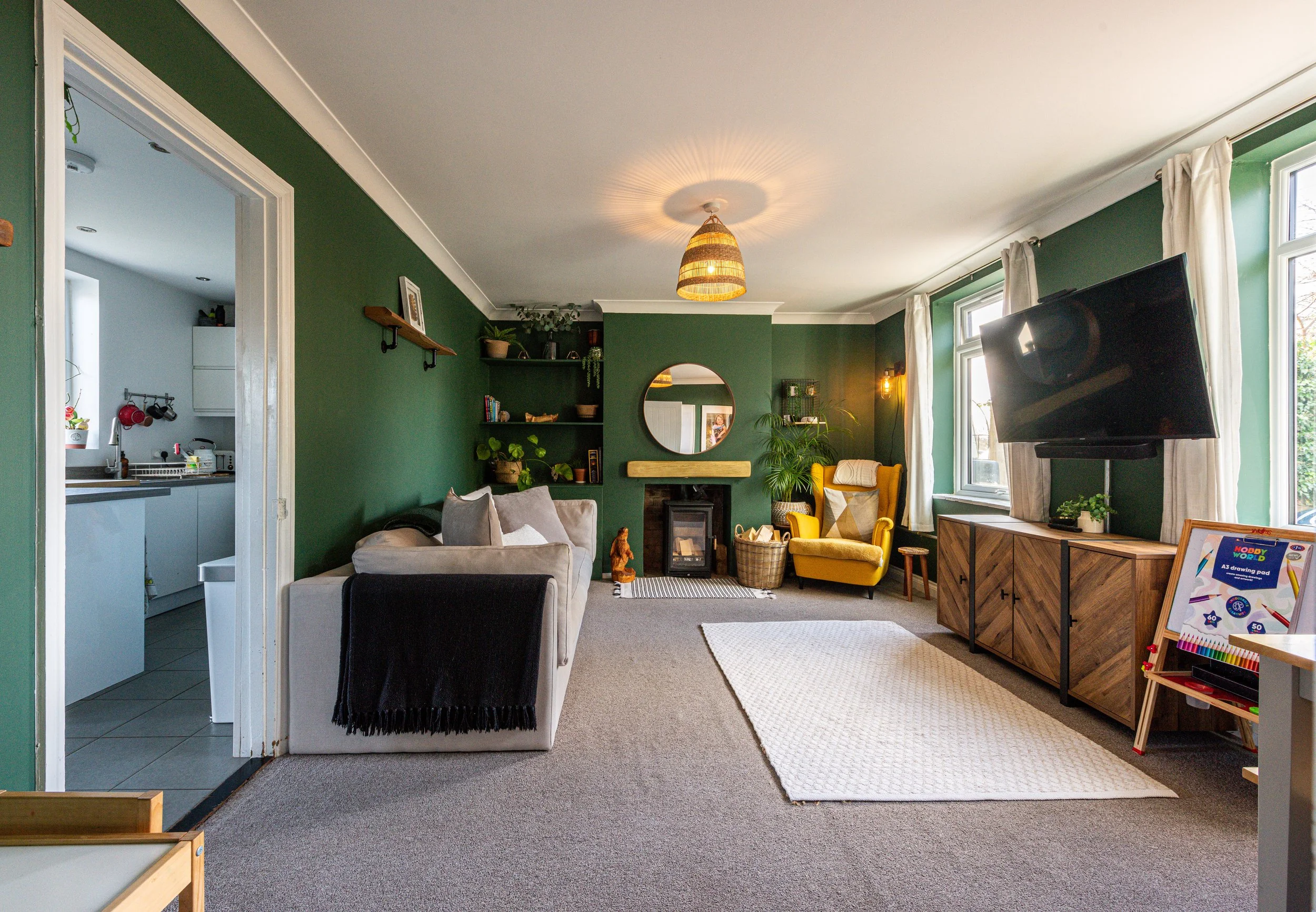 Living room with green walls, beige couch, yellow armchair, white rug, and flat-screen TV near large windows.