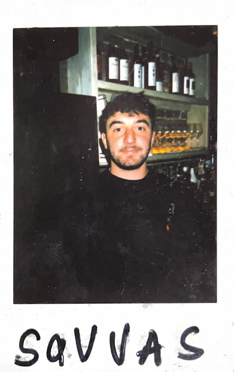 A man standing in front of shelves stocked with bottles and wine glasses.