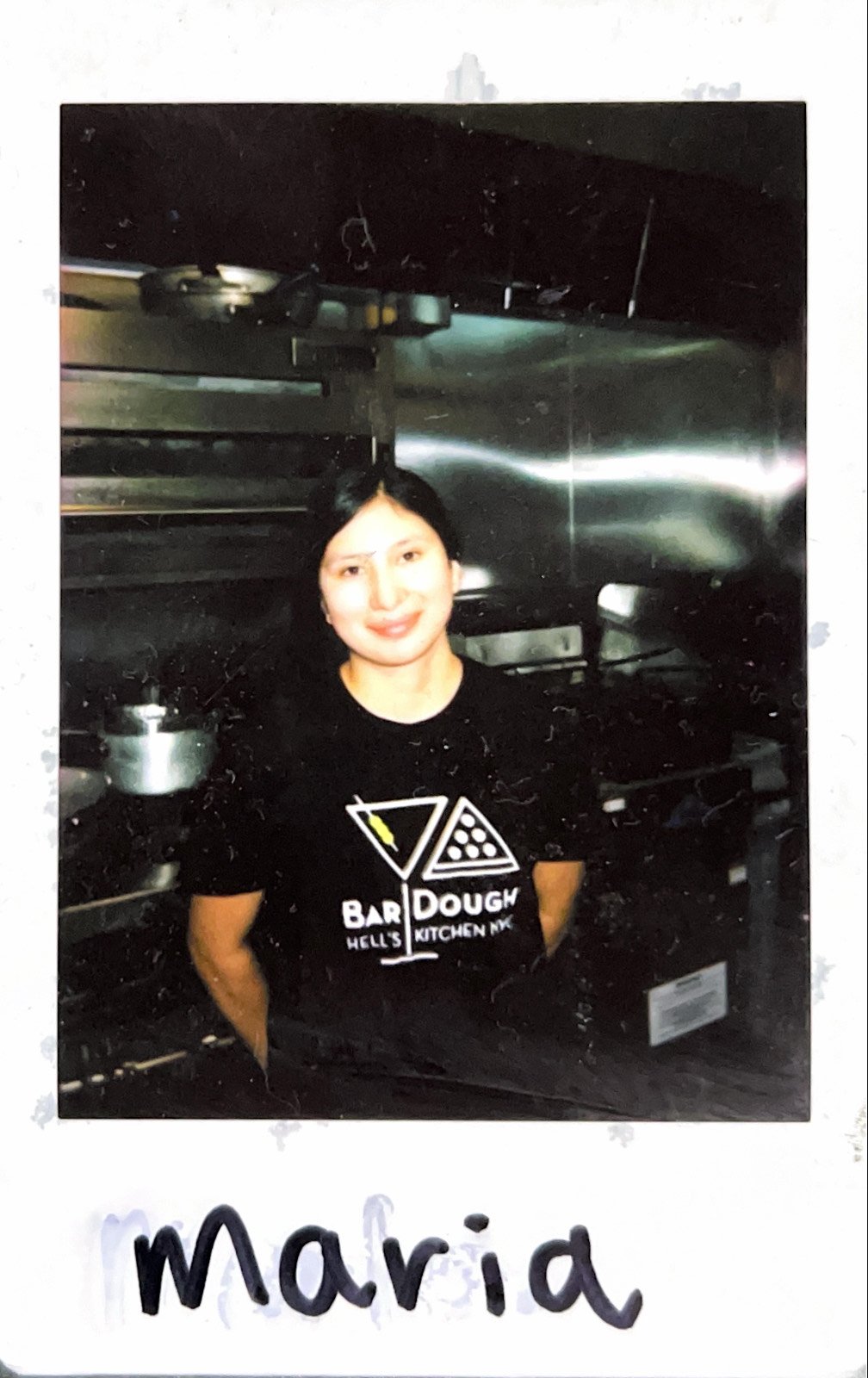 Person smiling in a kitchen wearing a "Bar Dough Hell's Kitchen NYC" t-shirt.