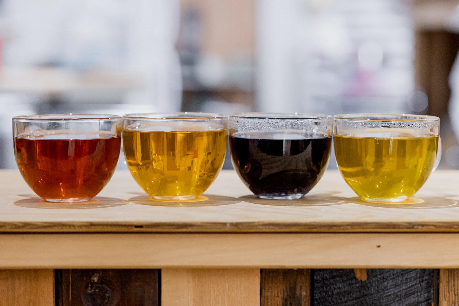 Four glasses of different colored drinks placed on a wooden surface.