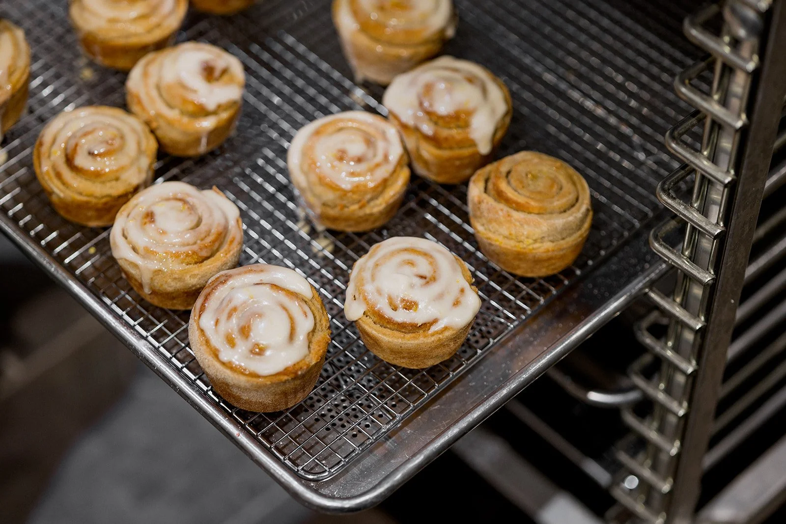 Freshly baked cinnamon rolls with icing on a metal cooling rack inside an oven or bakery display