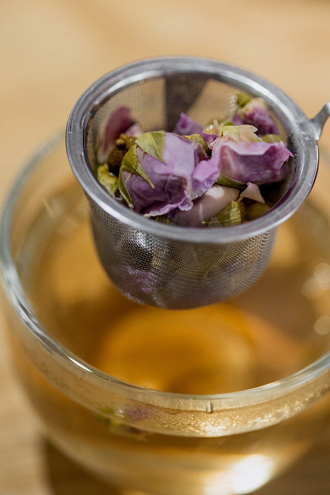 Close-up of a metal tea infuser filled with dried rose petals over a cup of hot tea.