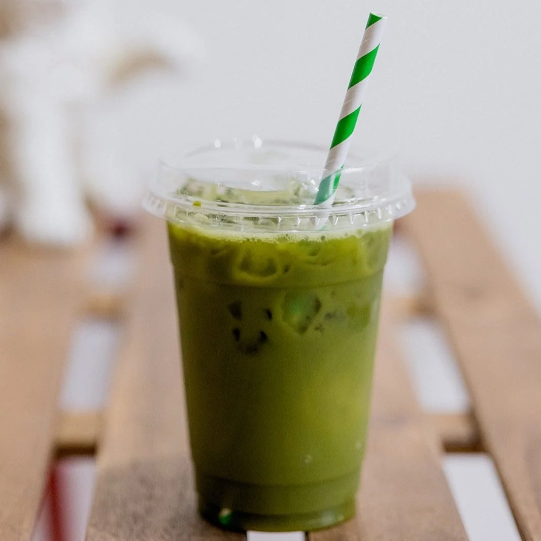 Green iced matcha latte with a striped straw in a plastic cup on a wooden table.