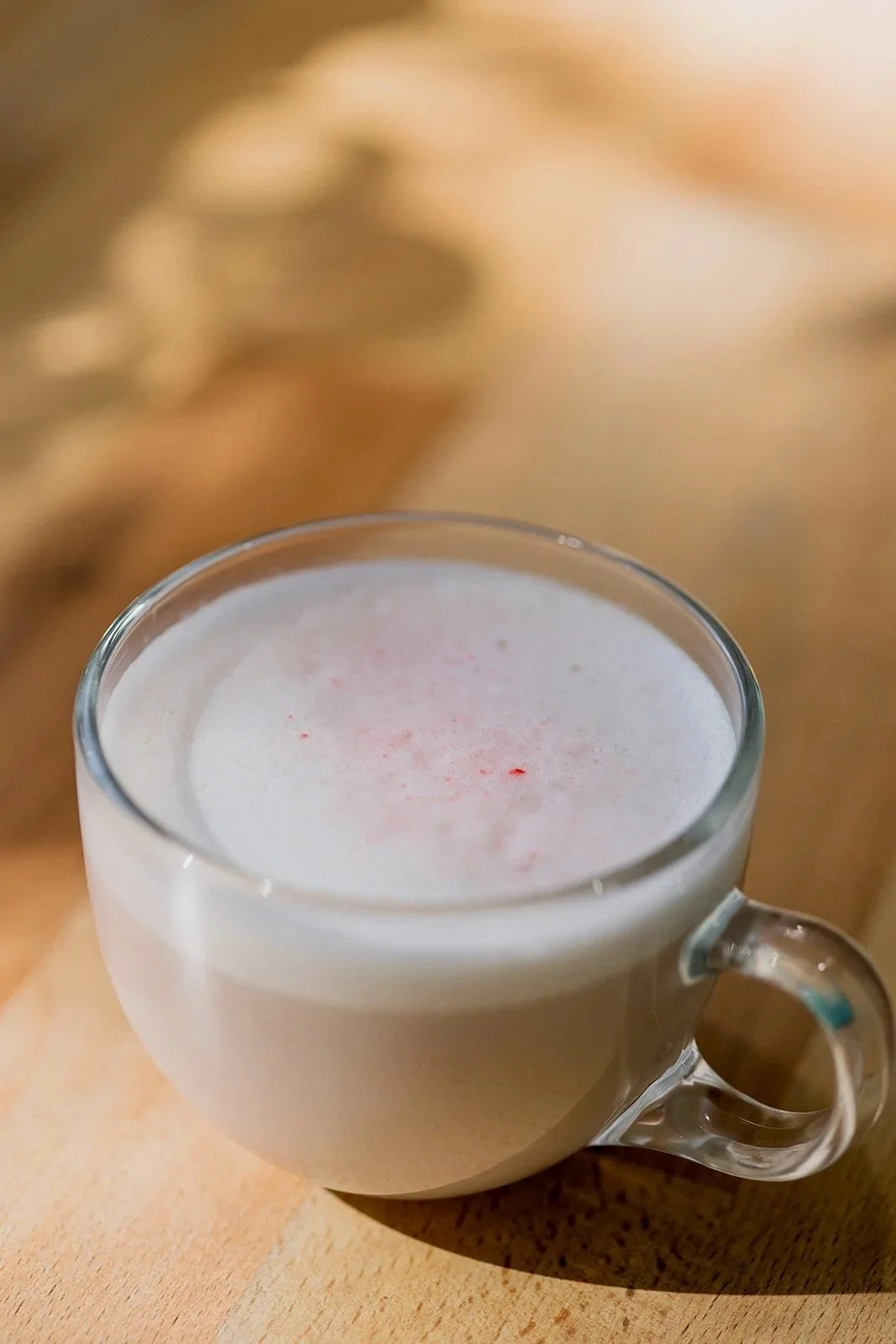 A clear glass cup filled with a frothy, white beverage, placed on a wooden surface, with a blurred background.