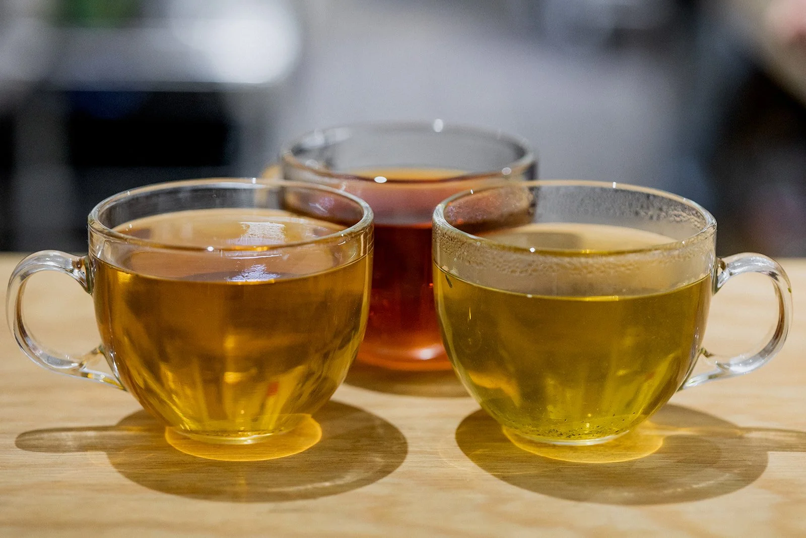 Three glass cups filled with tea on a wooden surface.