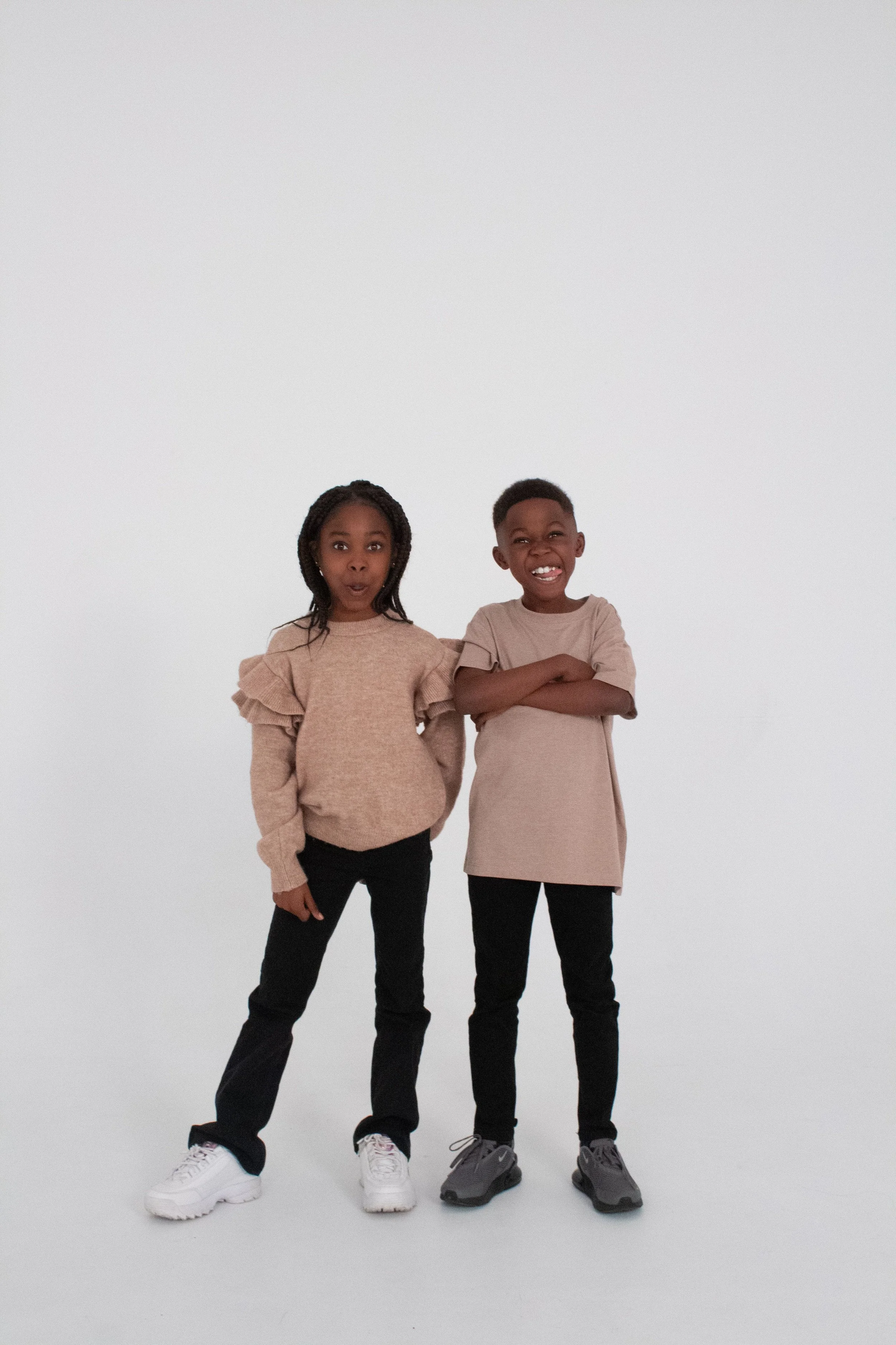 Two children, a girl and a boy, standing against a plain white background, making playful facial expressions.