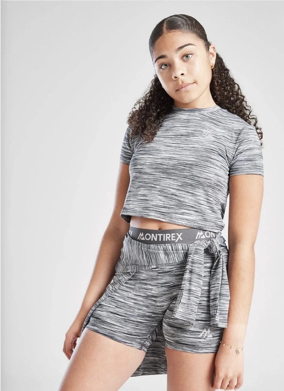 A young woman with curly hair wearing a matching striped athletic crop top and shorts, standing against a plain white background.