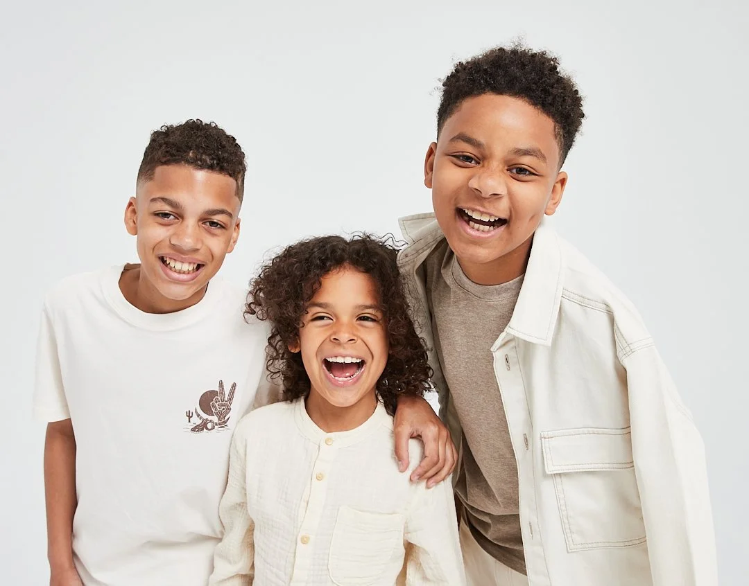 Three kids smiling and laughing together, close-up portrait against a plain light background.