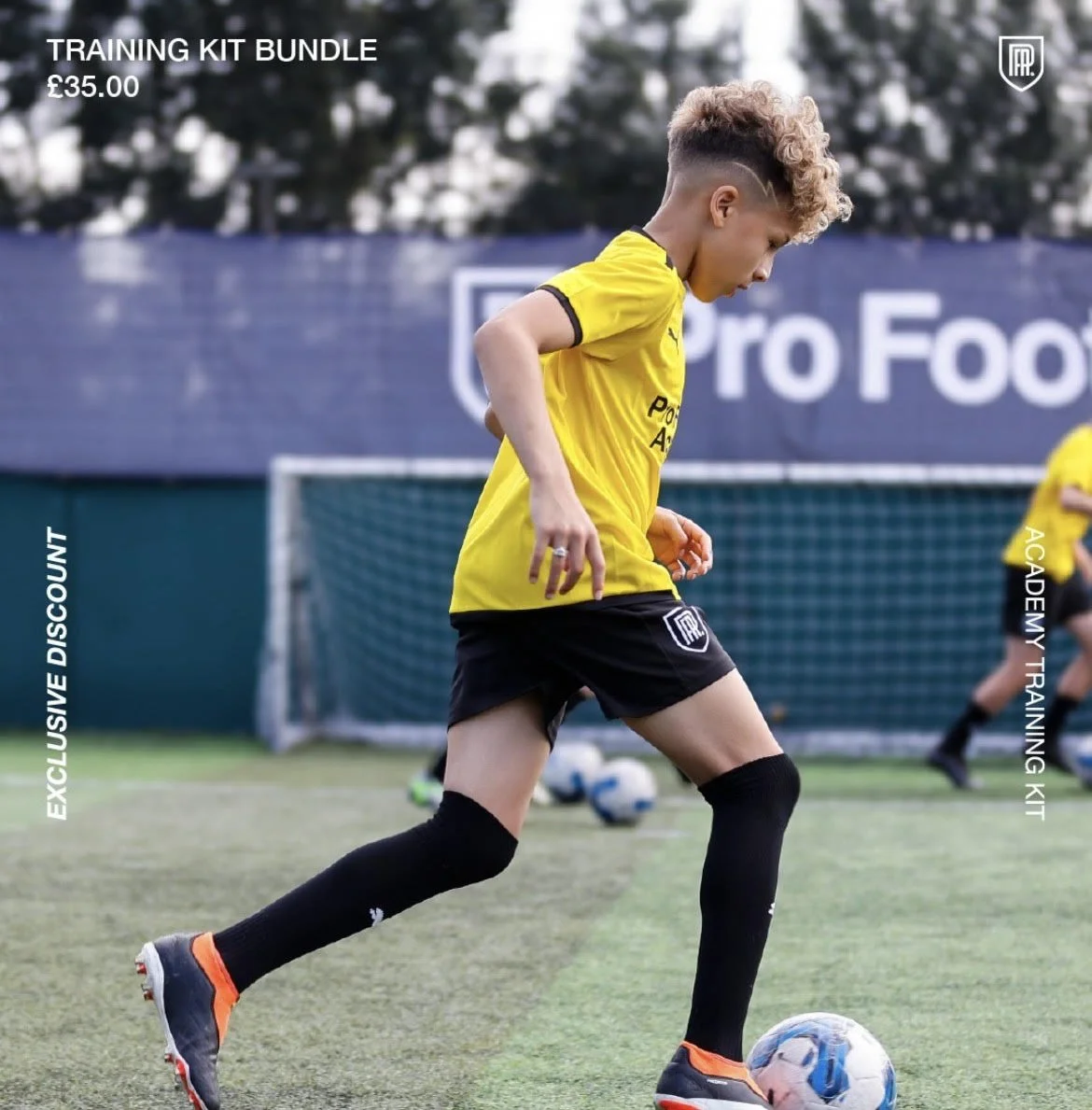 Young male soccer player in yellow jersey and black shorts dribbling a soccer ball on a field during training with a goalpost in the background.