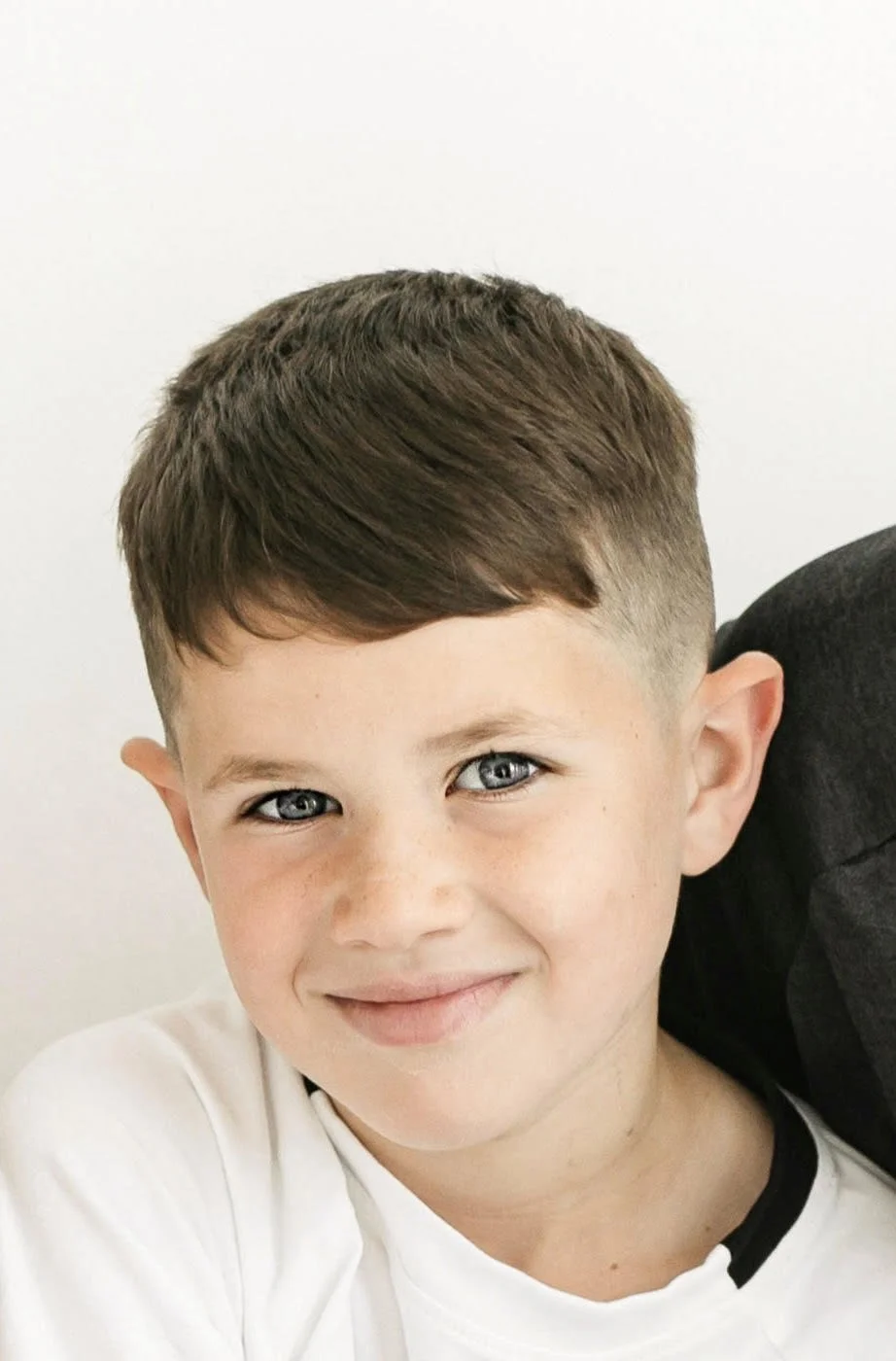 Close-up of a young boy with short brown hair, blue eyes, and a smile, against a plain white background.