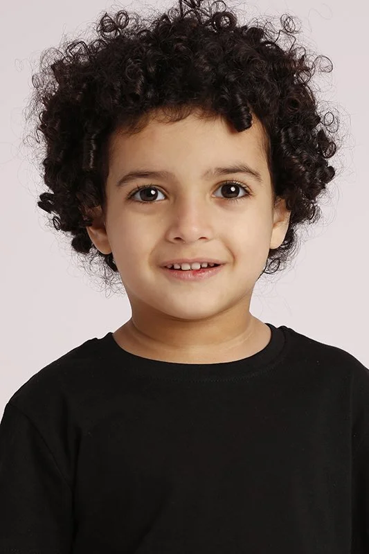 A young child with curly dark hair, brown eyes, and light skin, wearing a black shirt, smiling at the camera.