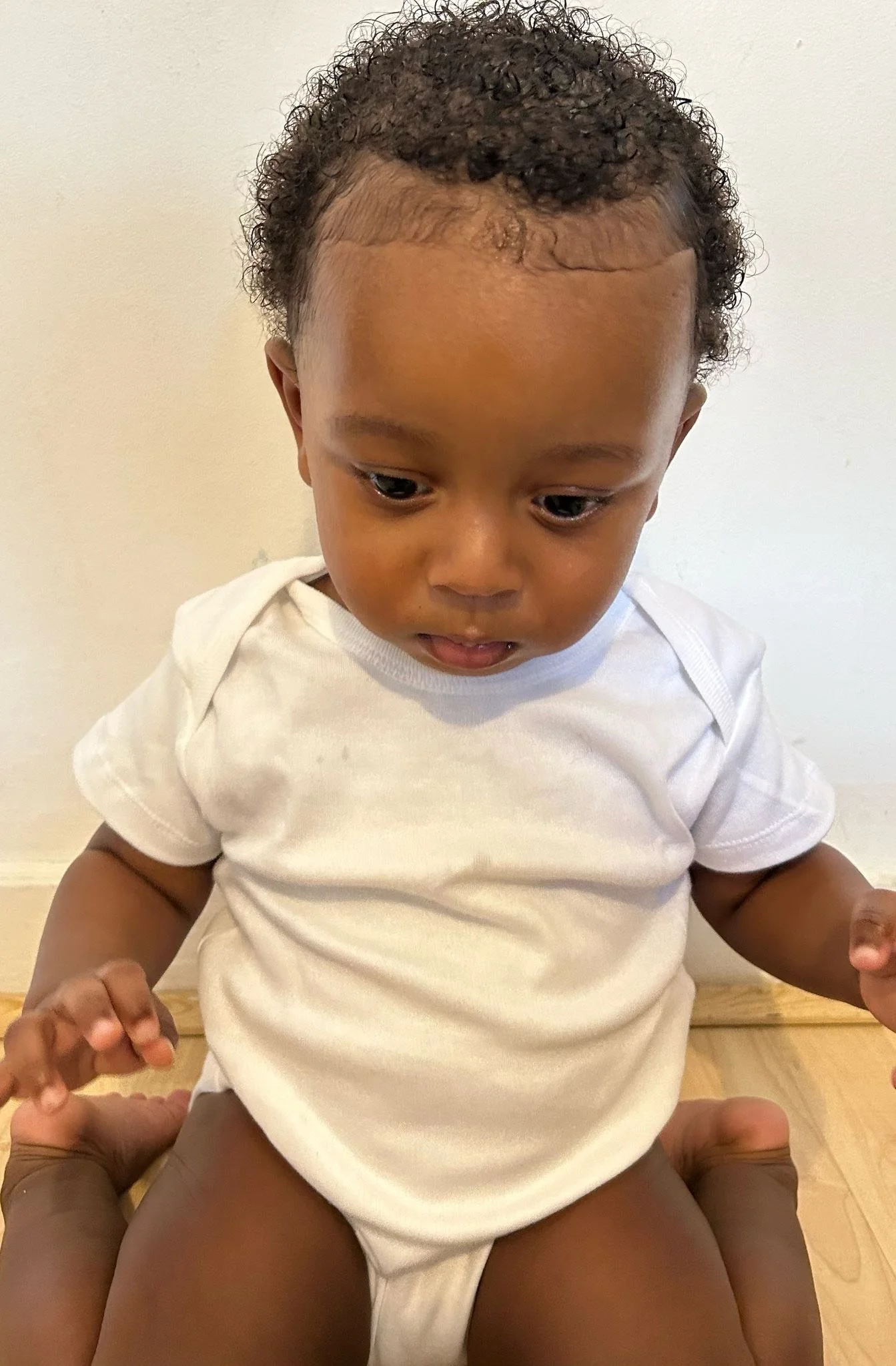 A young child with curly hair sitting on an adult's lap, looking downward. Modelling for leading child model and talent agency SocityUK based in London and Manchester.