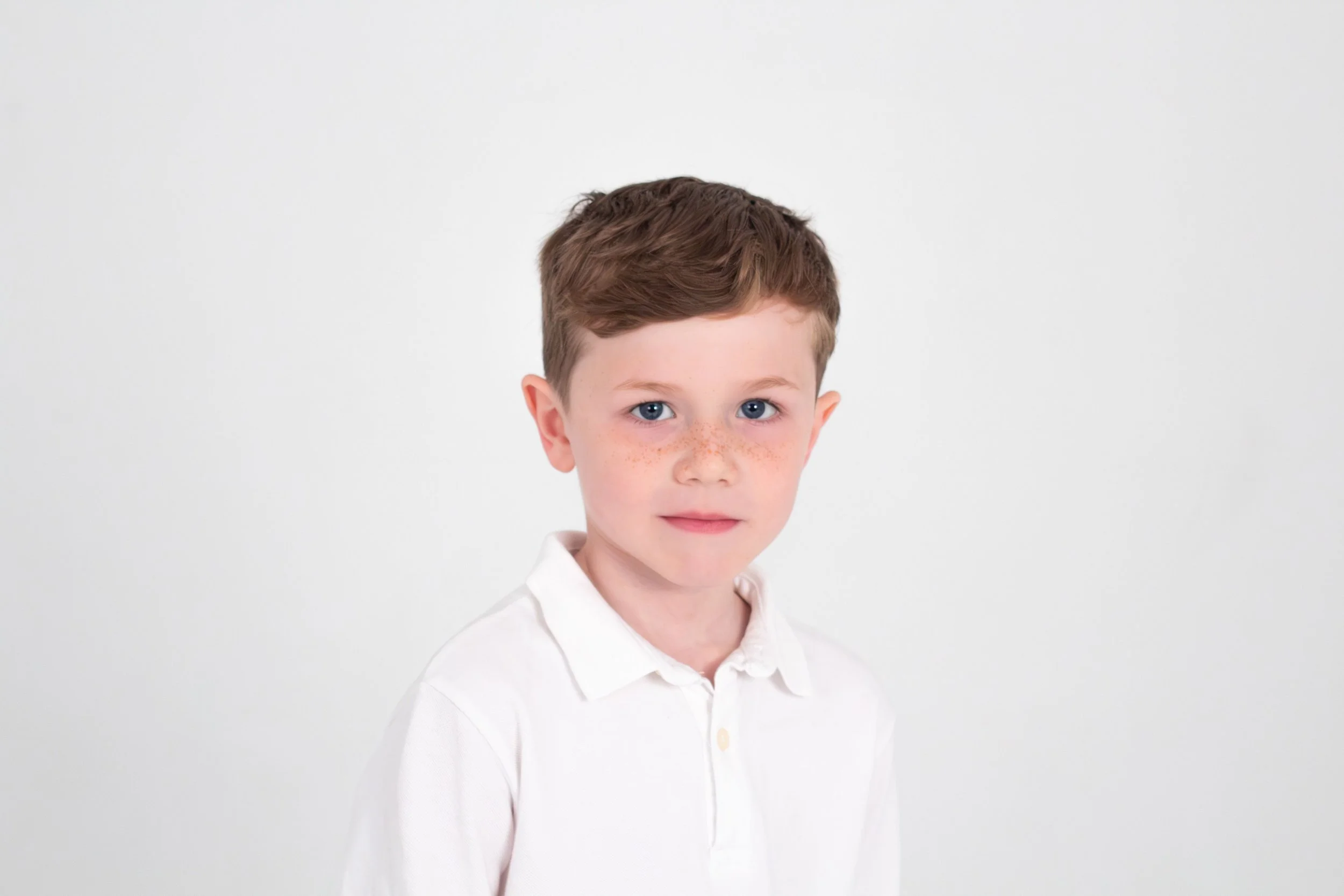 Young boy with brown hair, blue eyes, and freckles on his face, wearing a white collared shirt, against a plain white background.
