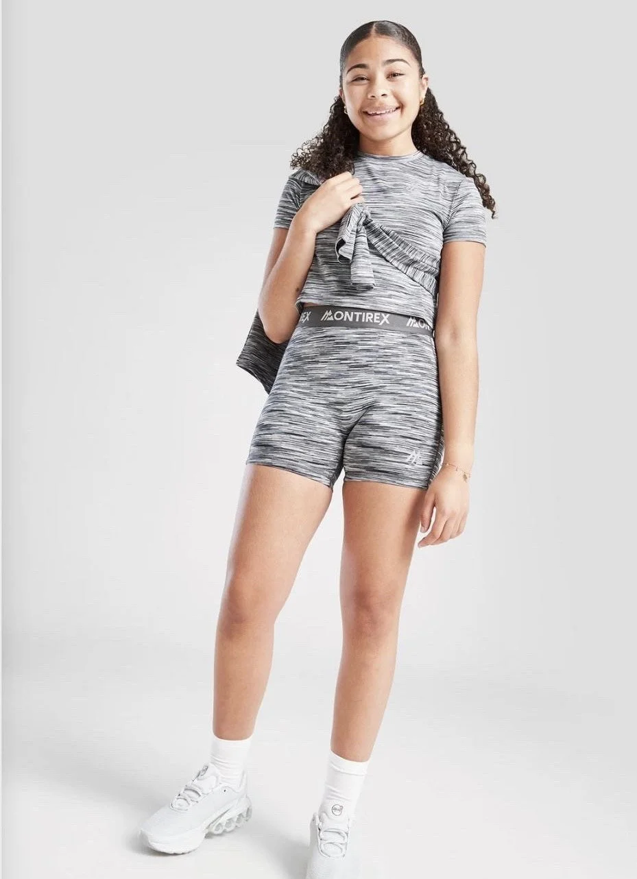 Young woman wearing gray and black athletic shorts and a matching t-shirt with a small knot at the chest, smiling and posing against a plain white background.