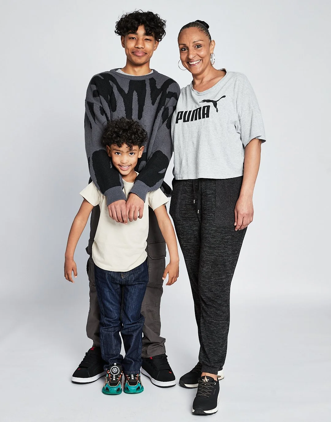 A woman and two young boys smiling and posing together in casual clothing against a plain background. Modelling for leading child model and talent agency SocityUK based in London and Manchester.