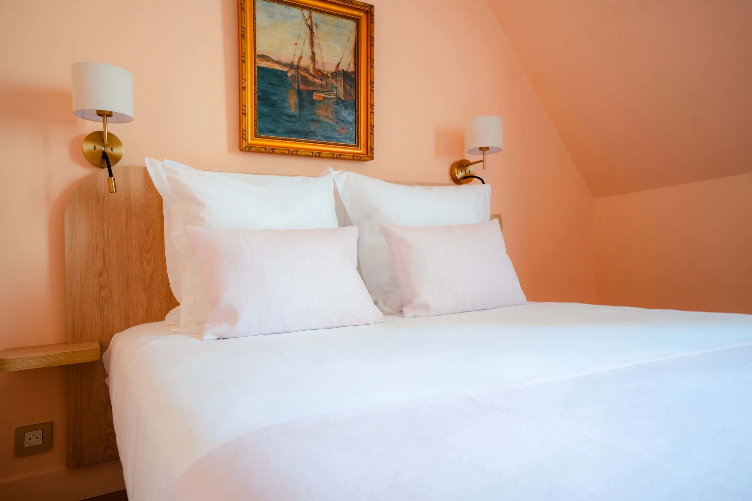 Chambre moderne avec un lit double, couvre-lit géométrique, fauteuil, lampe suspendue en rotin et table de chevet avec livre et lampe.