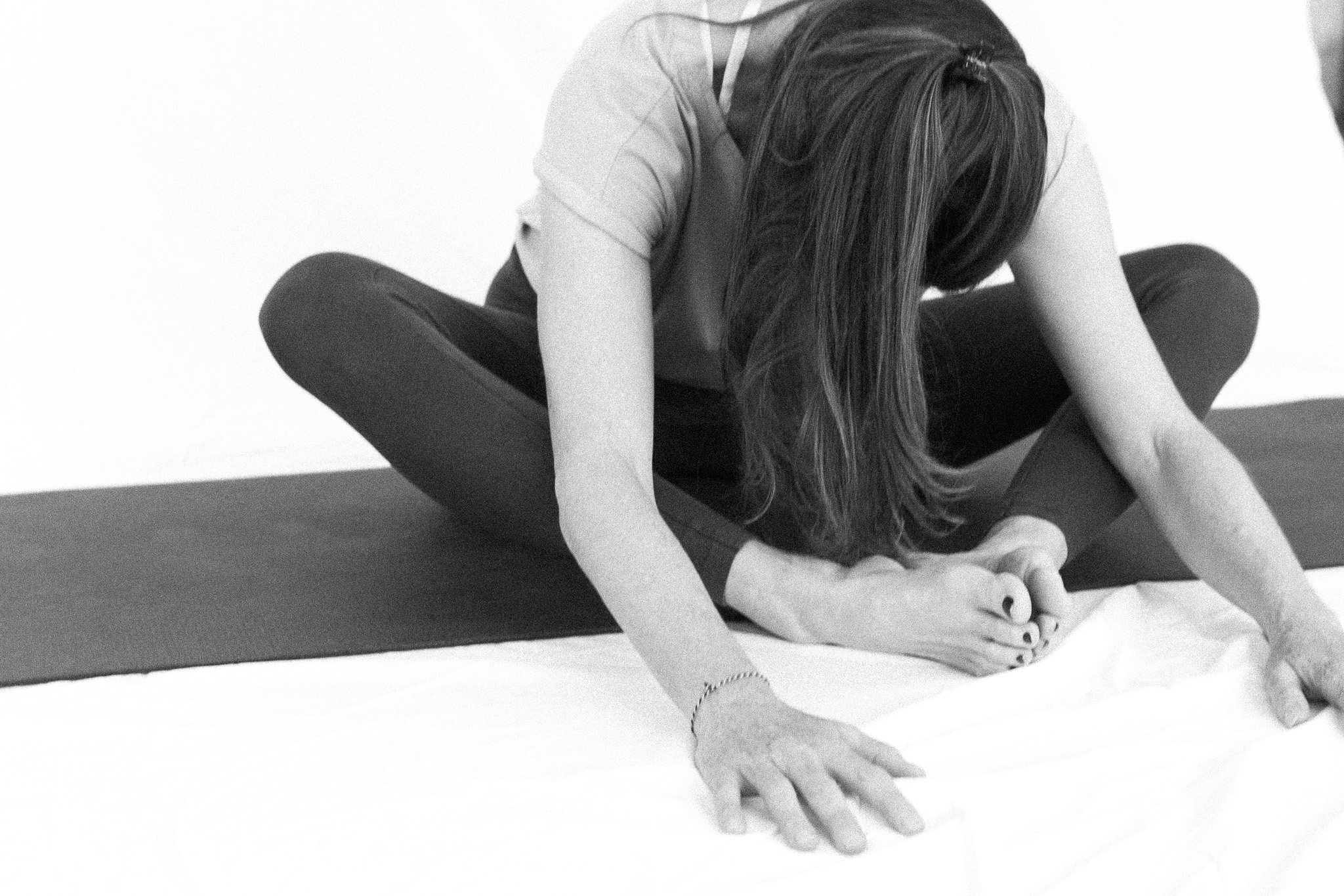 A woman practicing yoga, sitting cross-legged on a mat, stretching forward with her hands reaching towards her feet.
