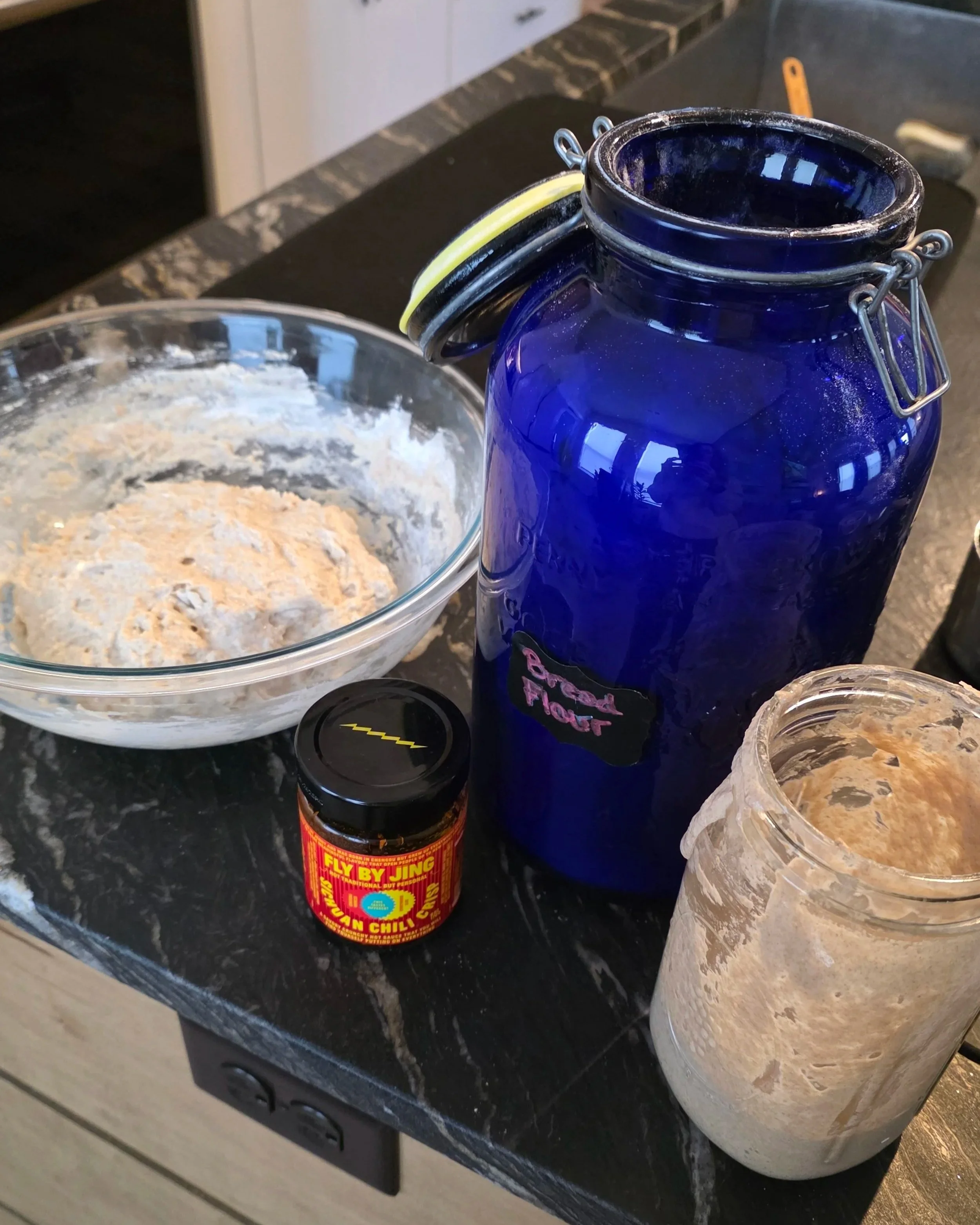 Active sourdough starter in ceramic crock with flour and sichuan chili crisp on counter