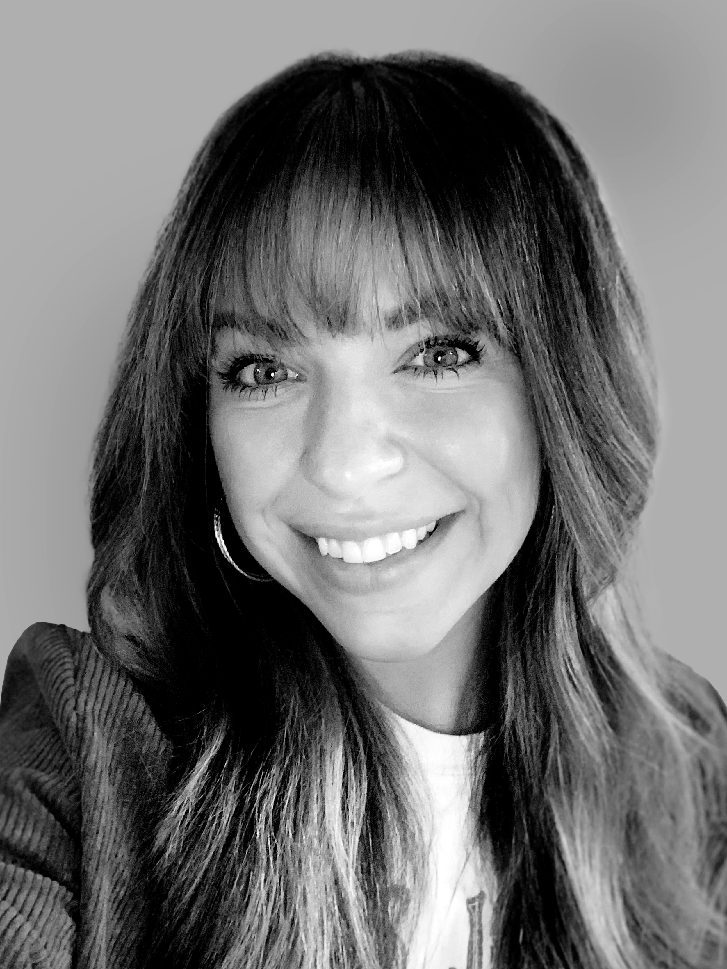 Black and white image of a person with long hair blowing across their face, wearing a dark shirt.