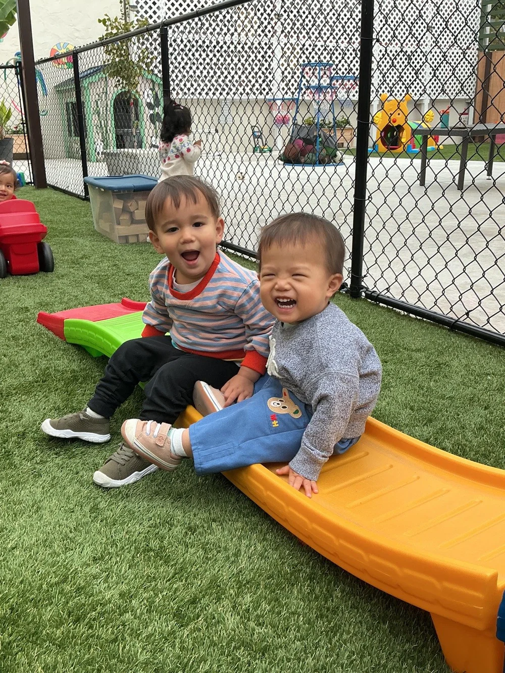 Two babies laughing on a little slide at the Center