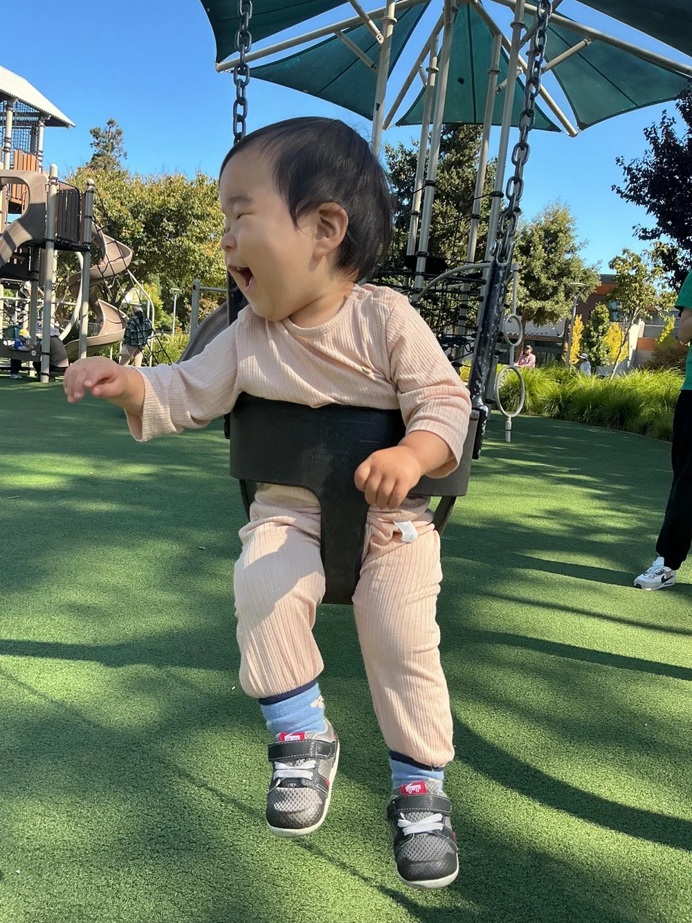 A toddler laughing on a swing at the park